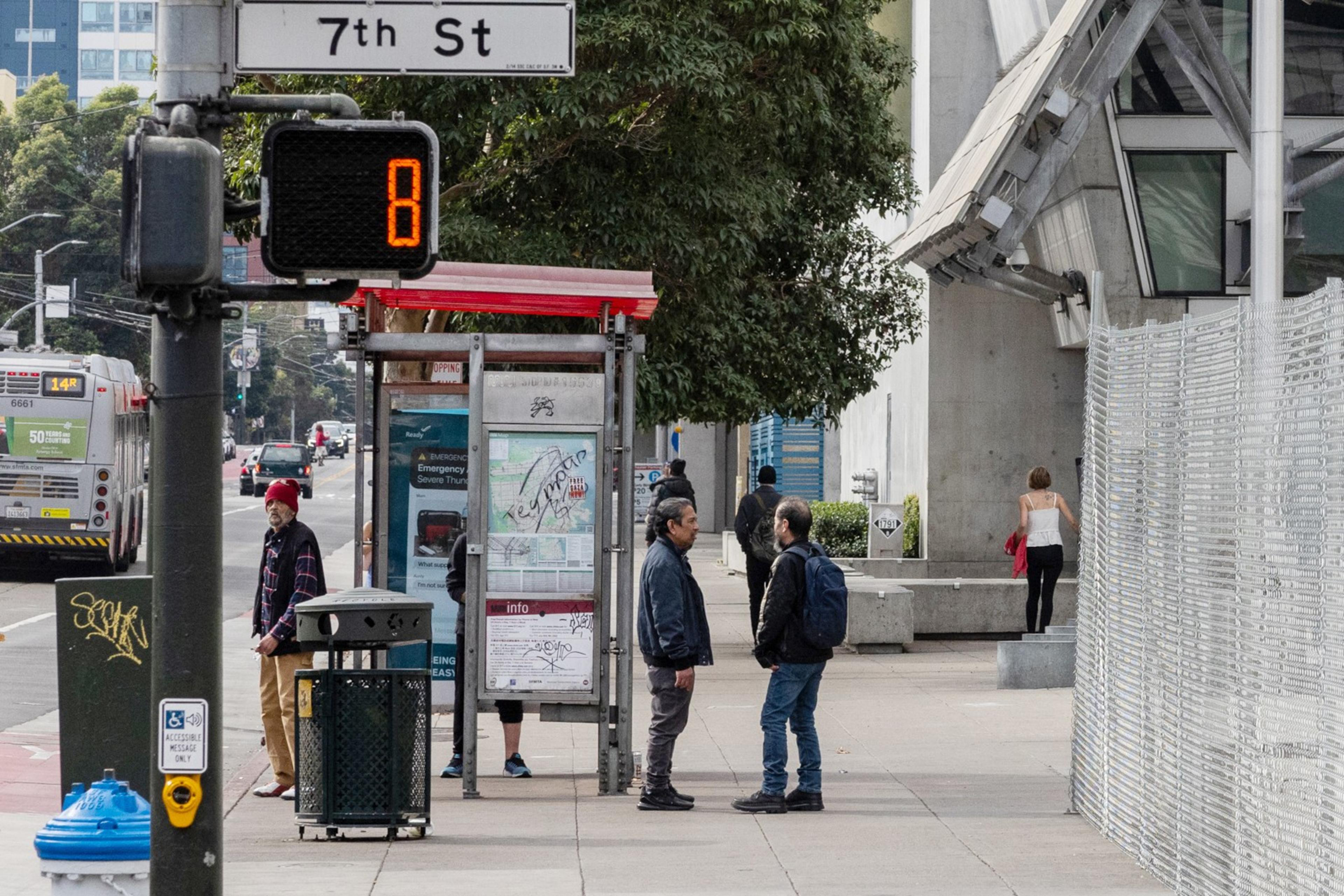 A few people stand on the sidewalk with a street sign that read 7th St.