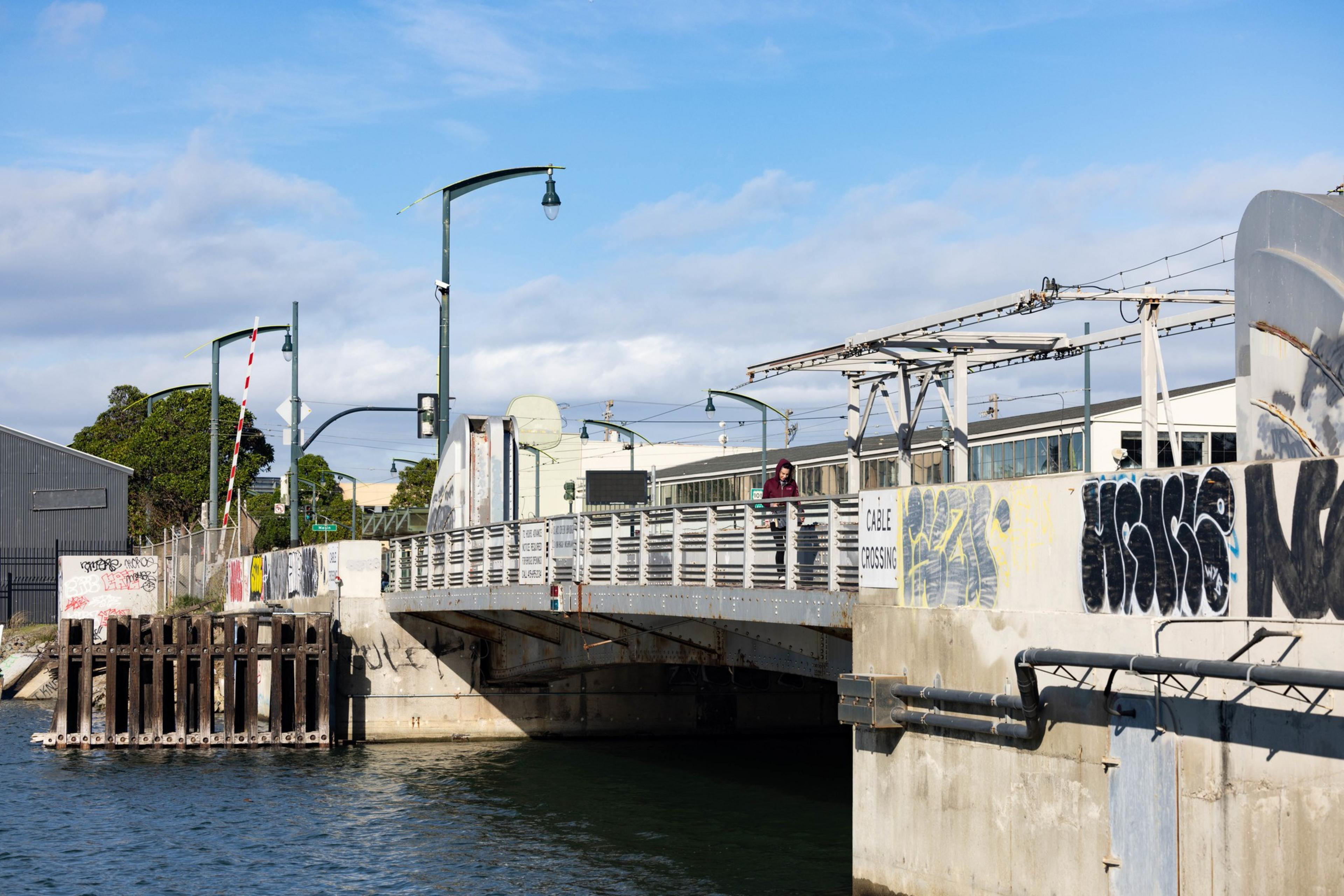 A steal bridge with person in a red hoodie walking over.