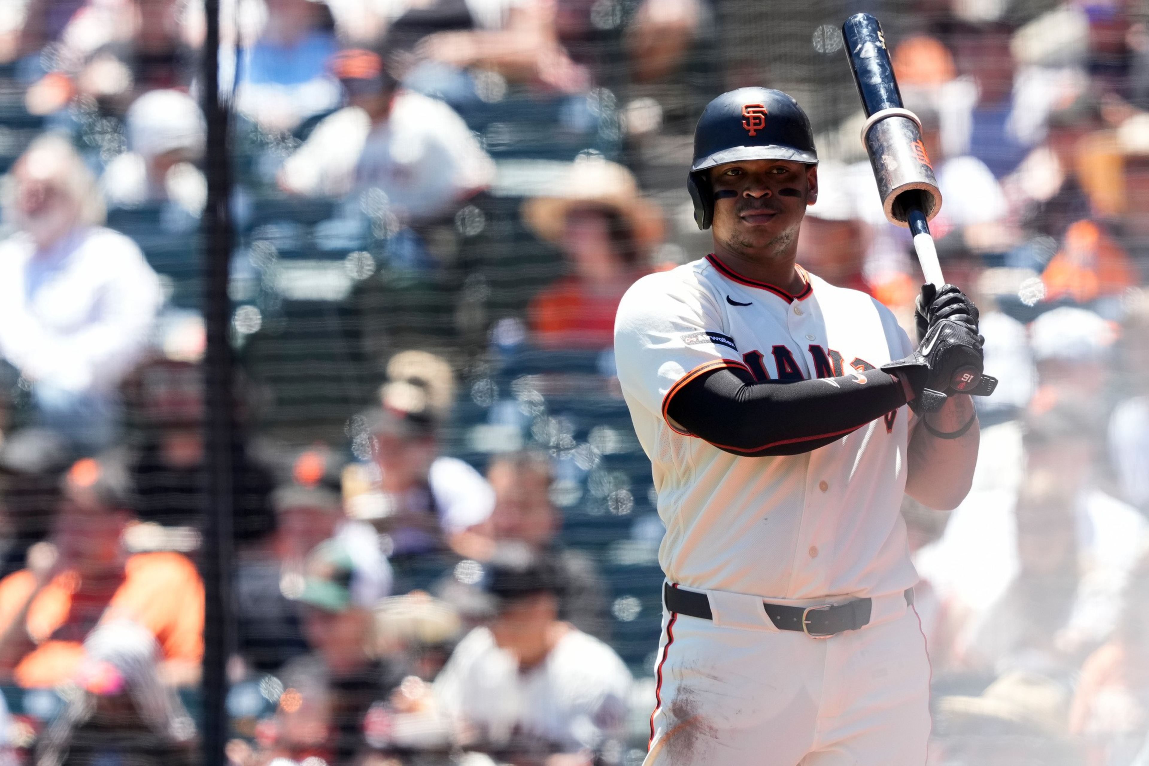 A baseball player from the San Francisco Giants stands ready to bat, wearing a helmet and white uniform with black and orange accents.