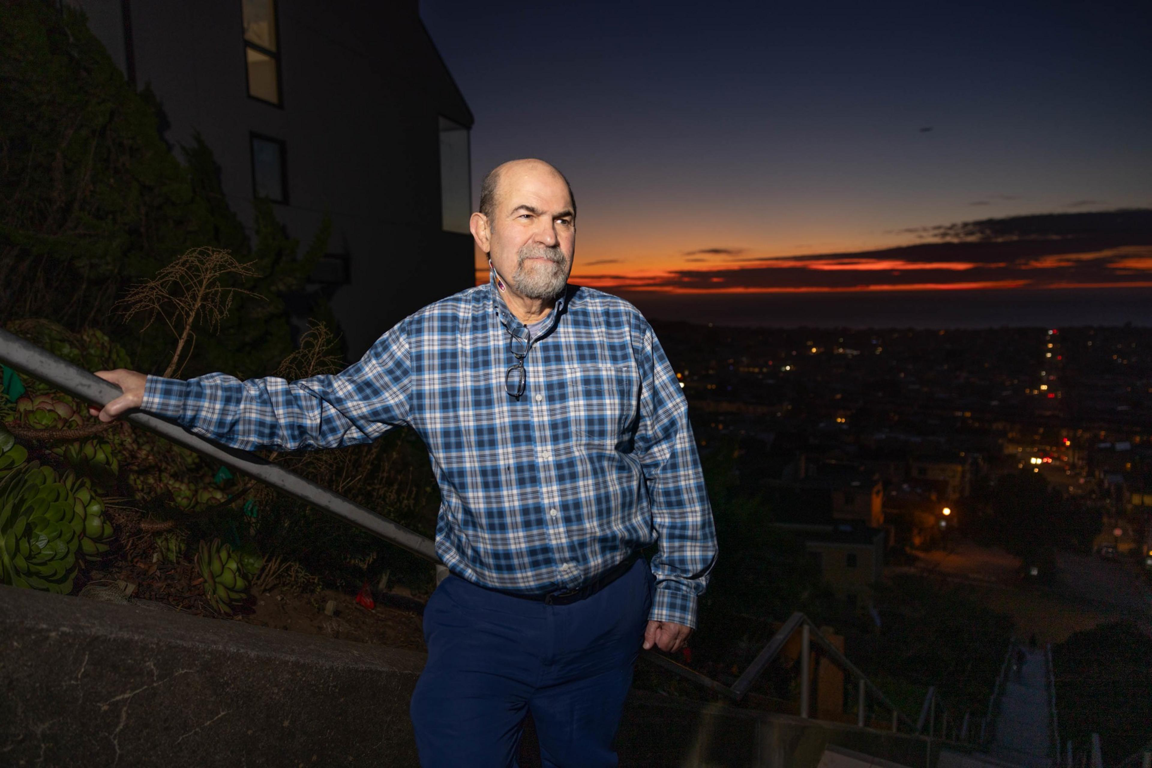 A man poses for a portrait on a long staircase during a sunset in the background.