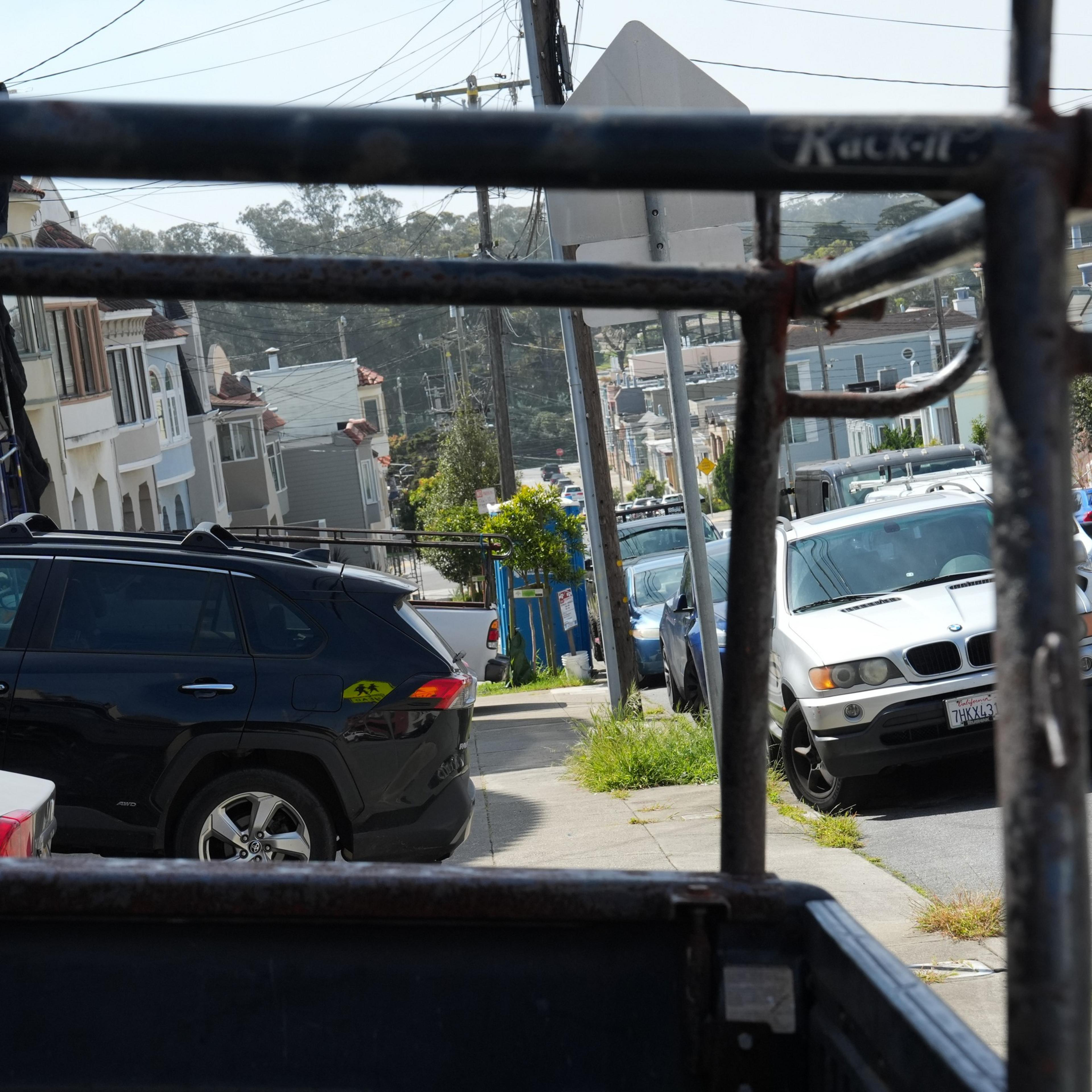 View from a cable car showing a sunny street lined with cars and houses.
