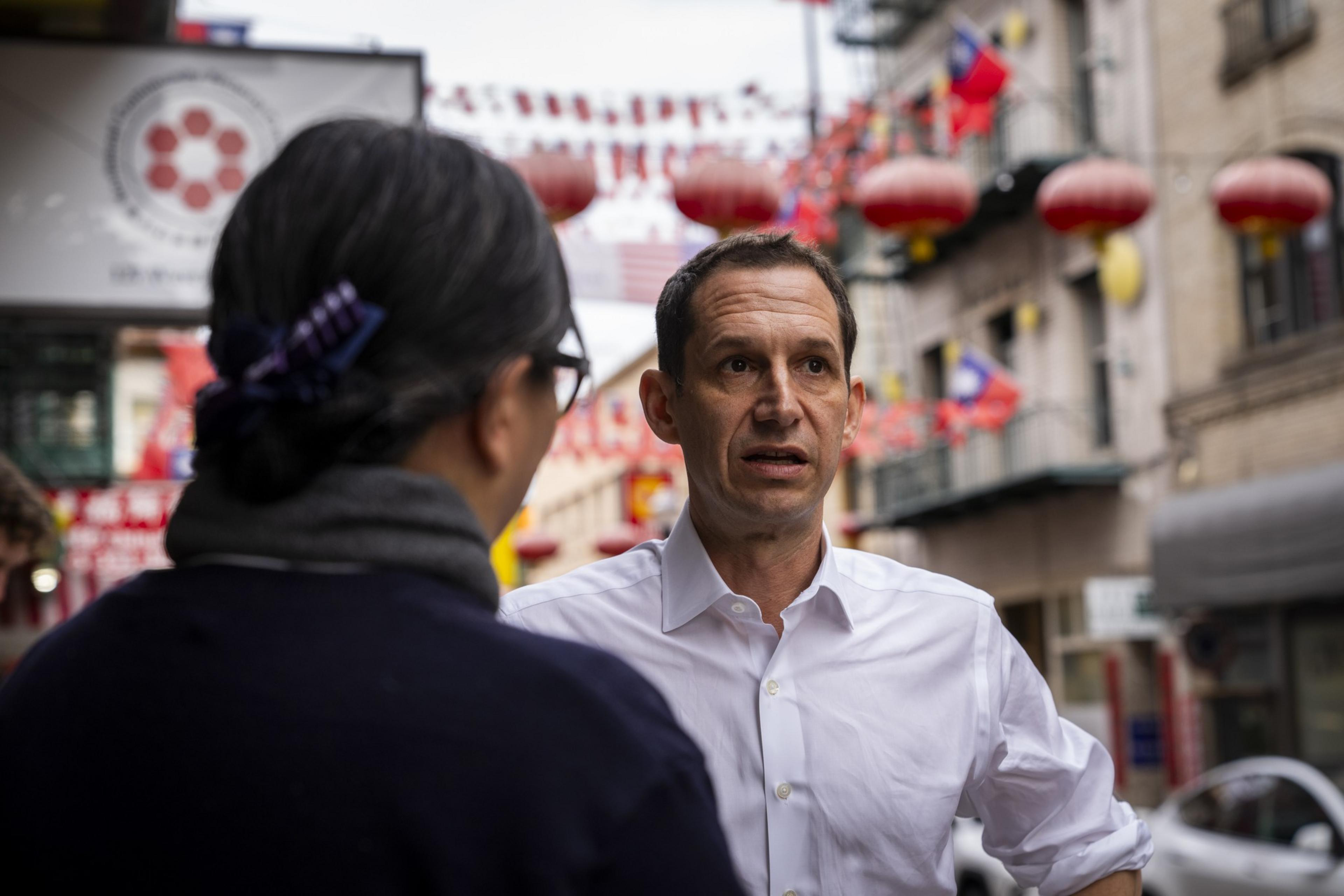 A man converses with someone in a street lined with red lanterns and festive flags.