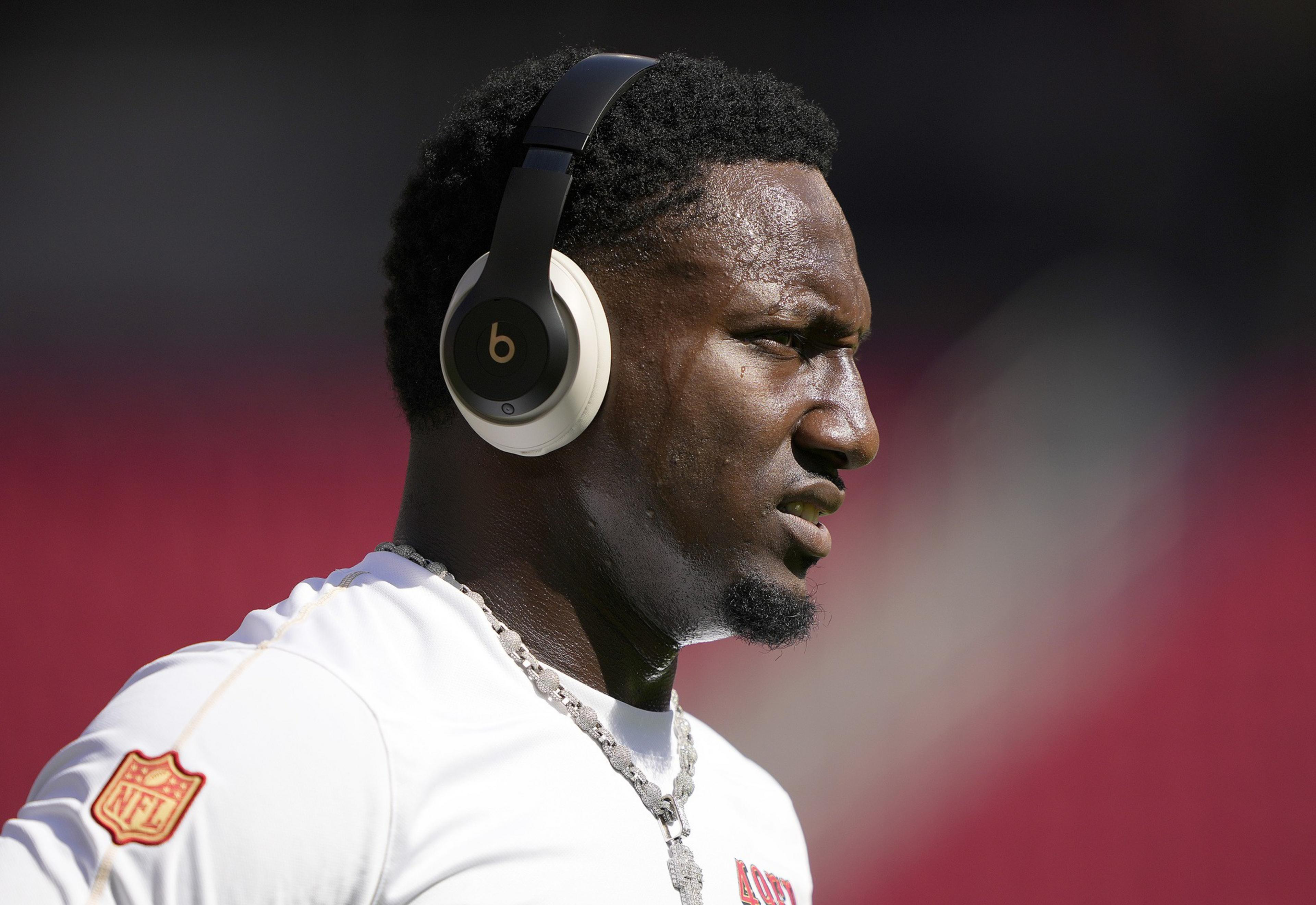 A man wearing large black headphones is outdoors. He's in profile view, wearing a white shirt with an NFL patch, focused and seemingly in mid-motion.