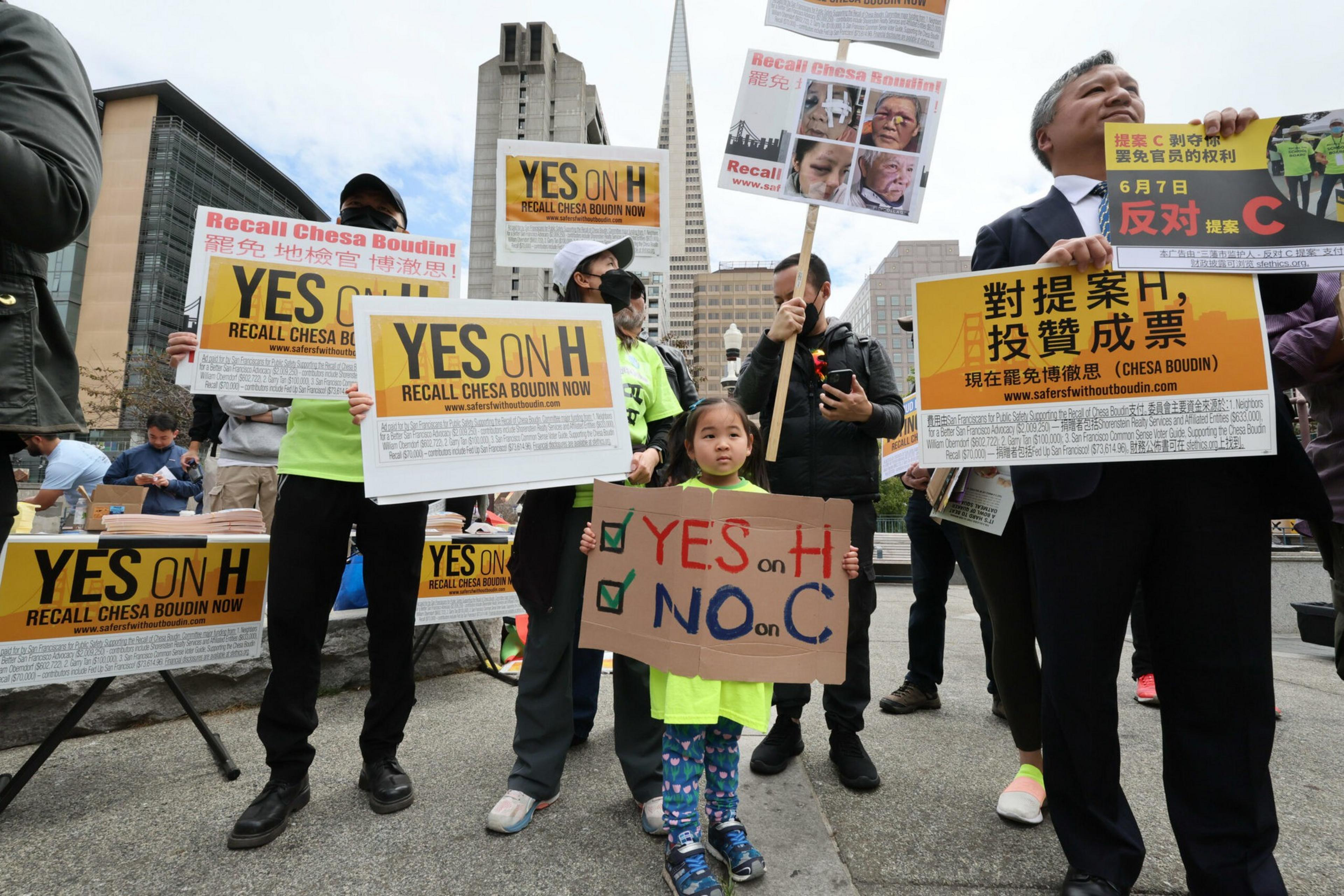 People hold signs advocating to "Recall Chesa Boudin" and vote "YES on H" and "NO on C," with some signs in English and others in Chinese characters.