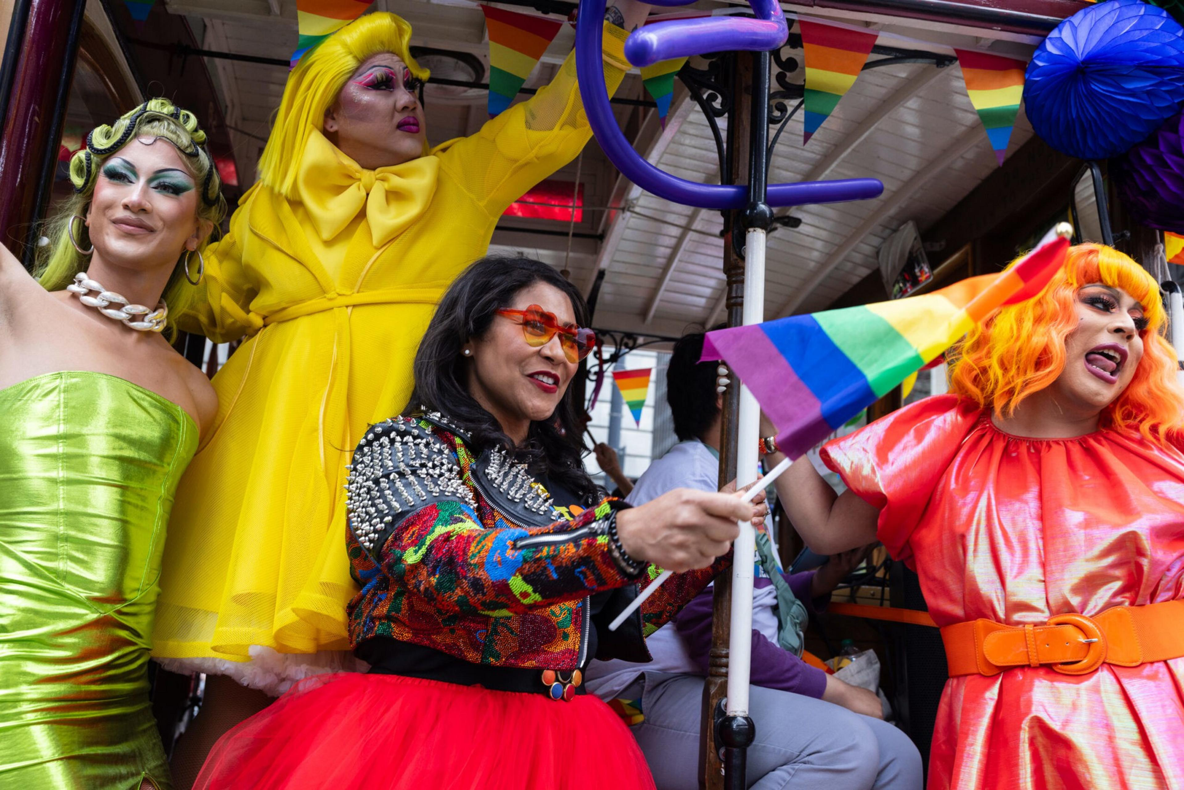Four people dressed in colorful, vibrant outfits celebrate with rainbow flags and decorations at a lively event.