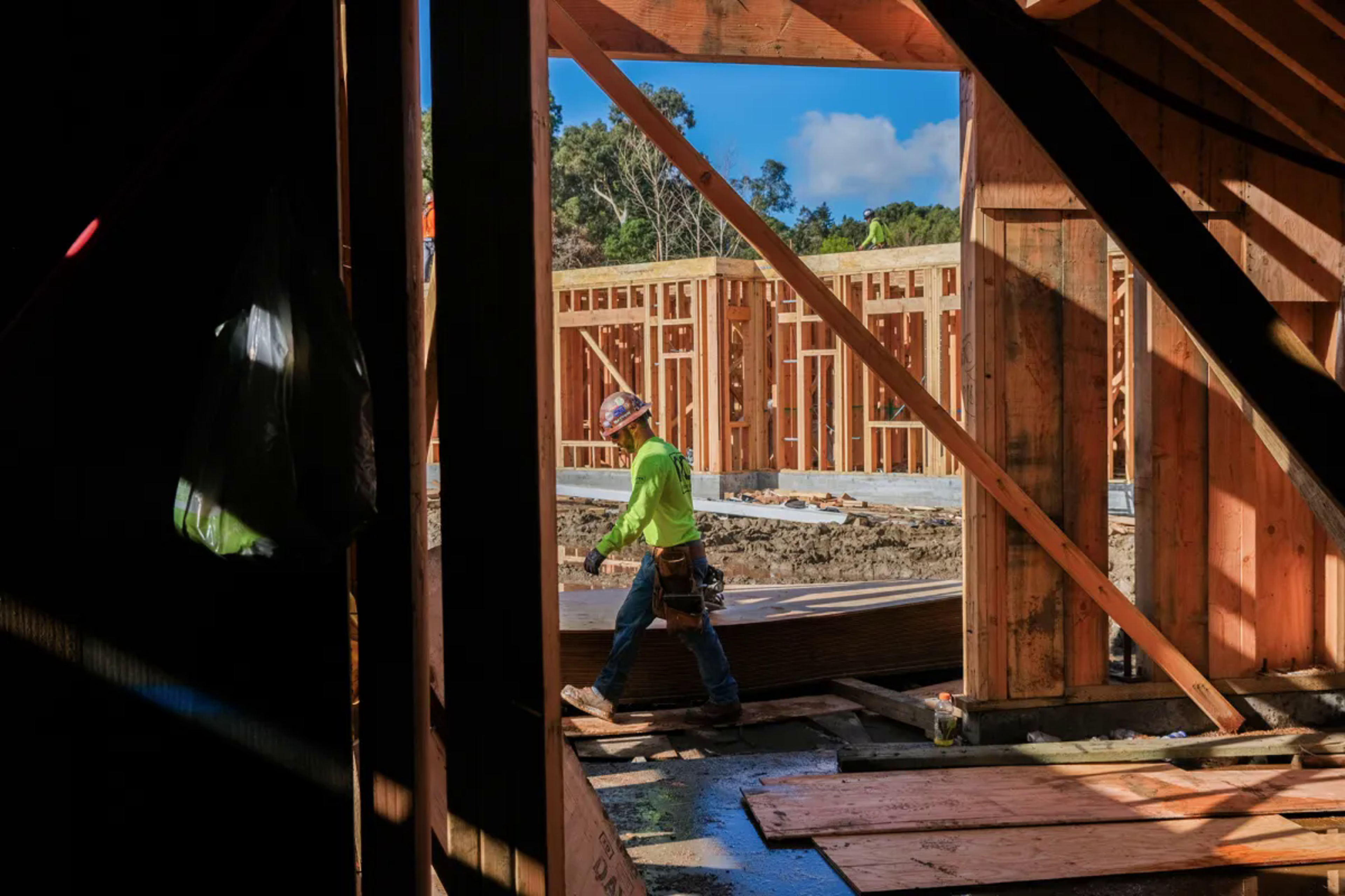 Man in hard hat walks through construction site with wooden structures in the foreground and background