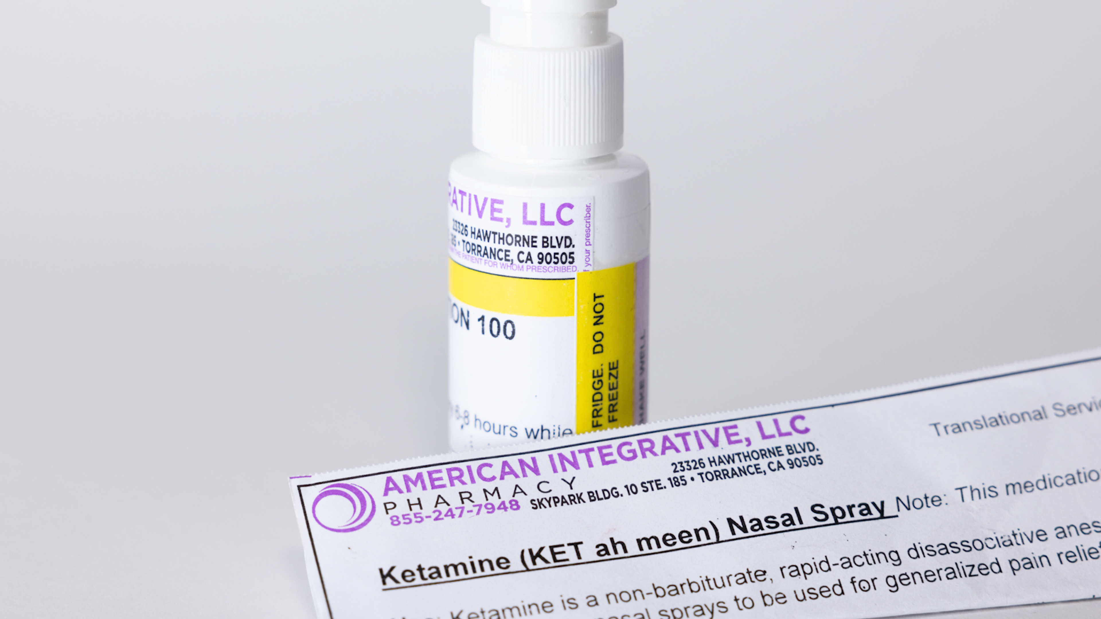 A white nasal spray bottle with a yellow "DO NOT FREEZE" label and a pharmacy paper detailing "Ketamine Nasal Spray" from American Integrative Pharmacy.