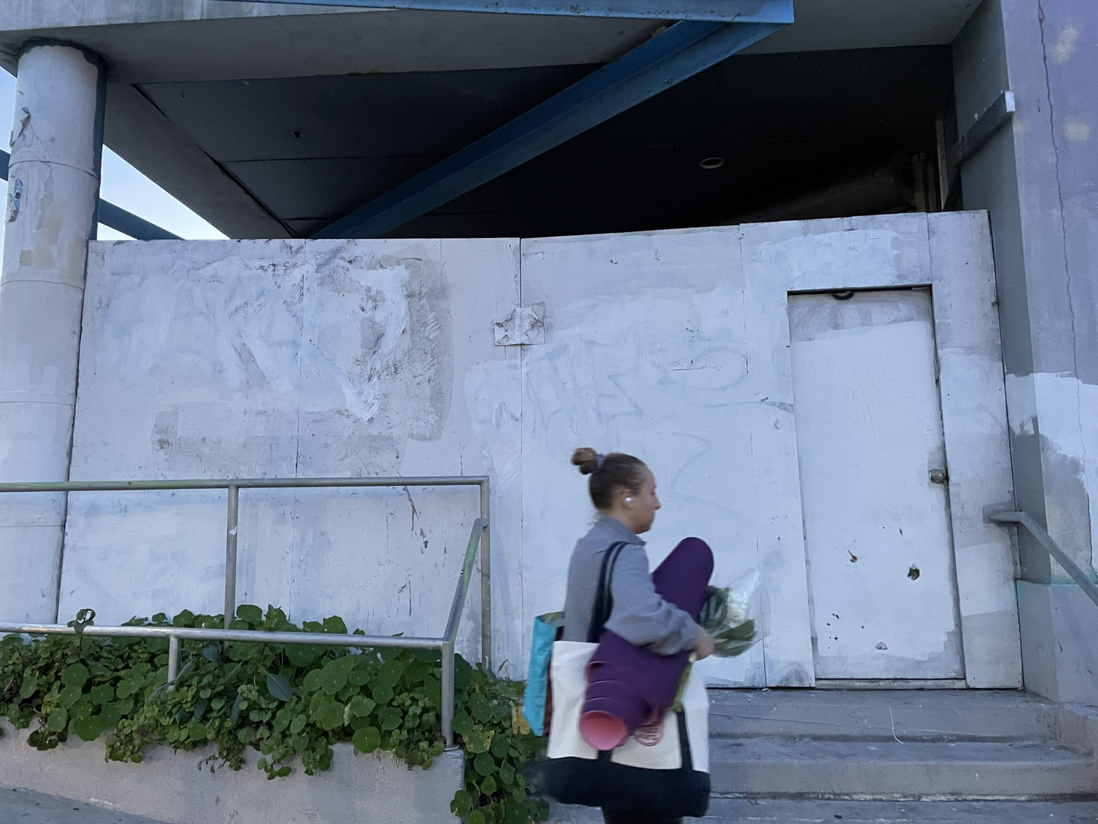 A woman walks in front of a boarded-up store entrance.