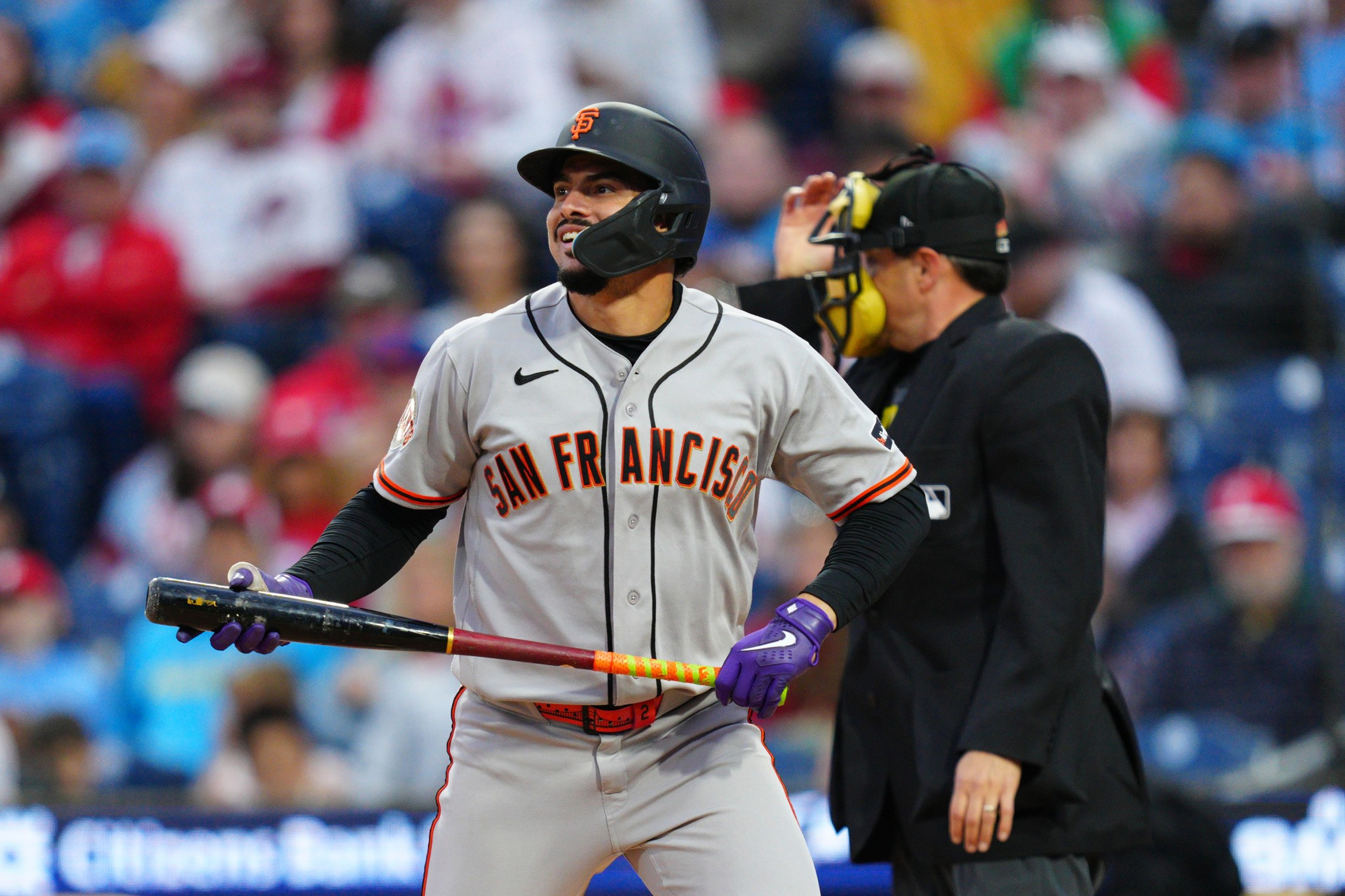 A San Francisco Giants baseball player stands with a bat, looking up, while the umpire behind him adjusts his mask.