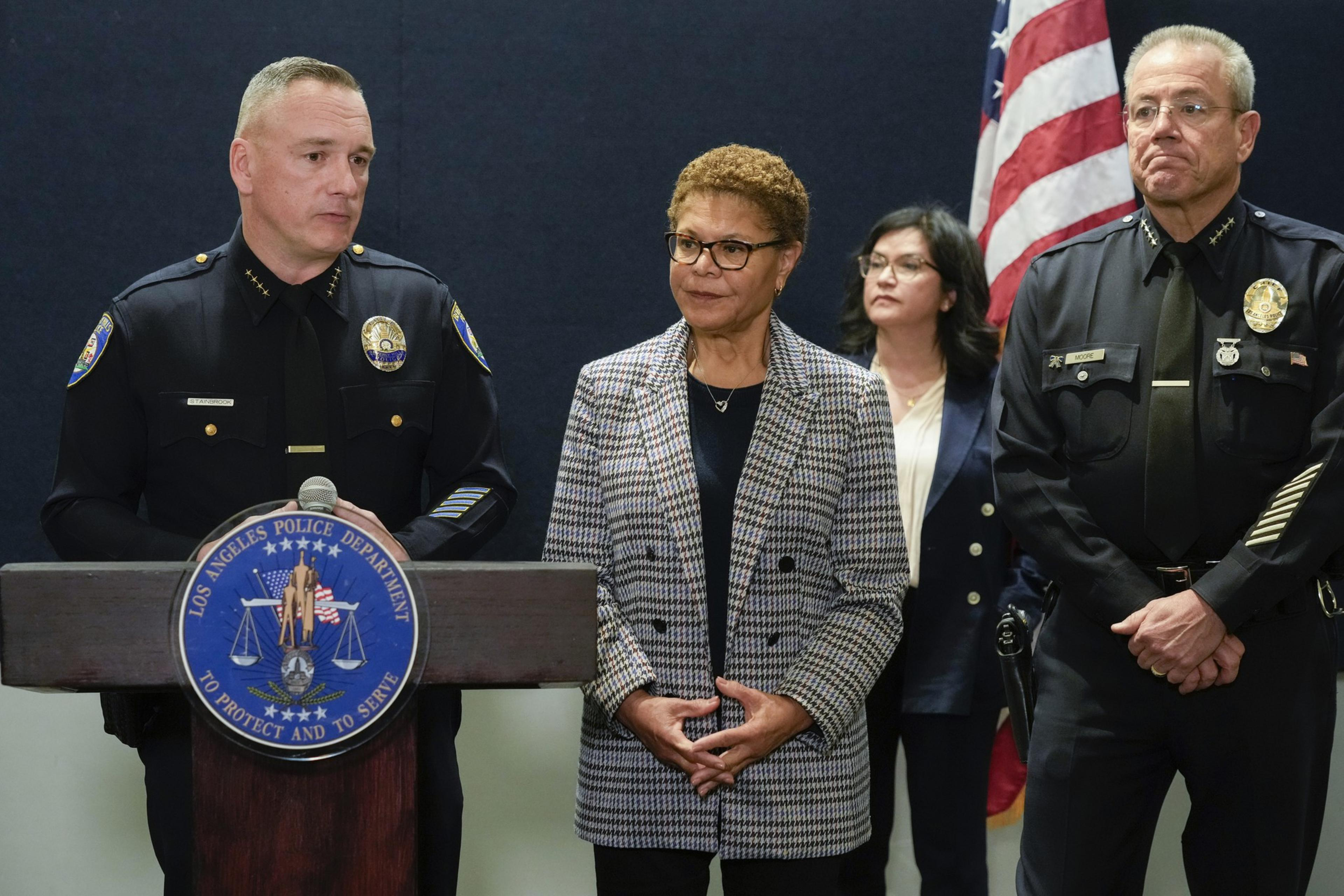 A man in a police uniform stands behind a podium with three other people standing directly to his left.