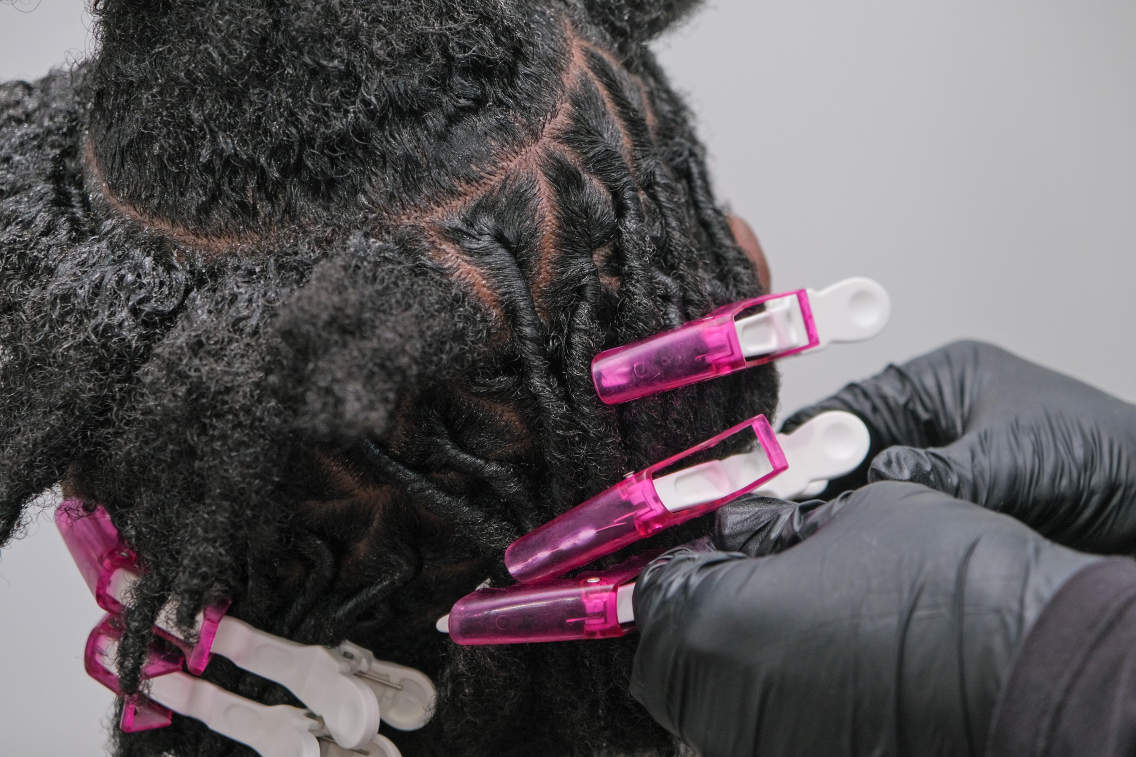 A hand in a black glove is styling textured hair with pink hair clips.
