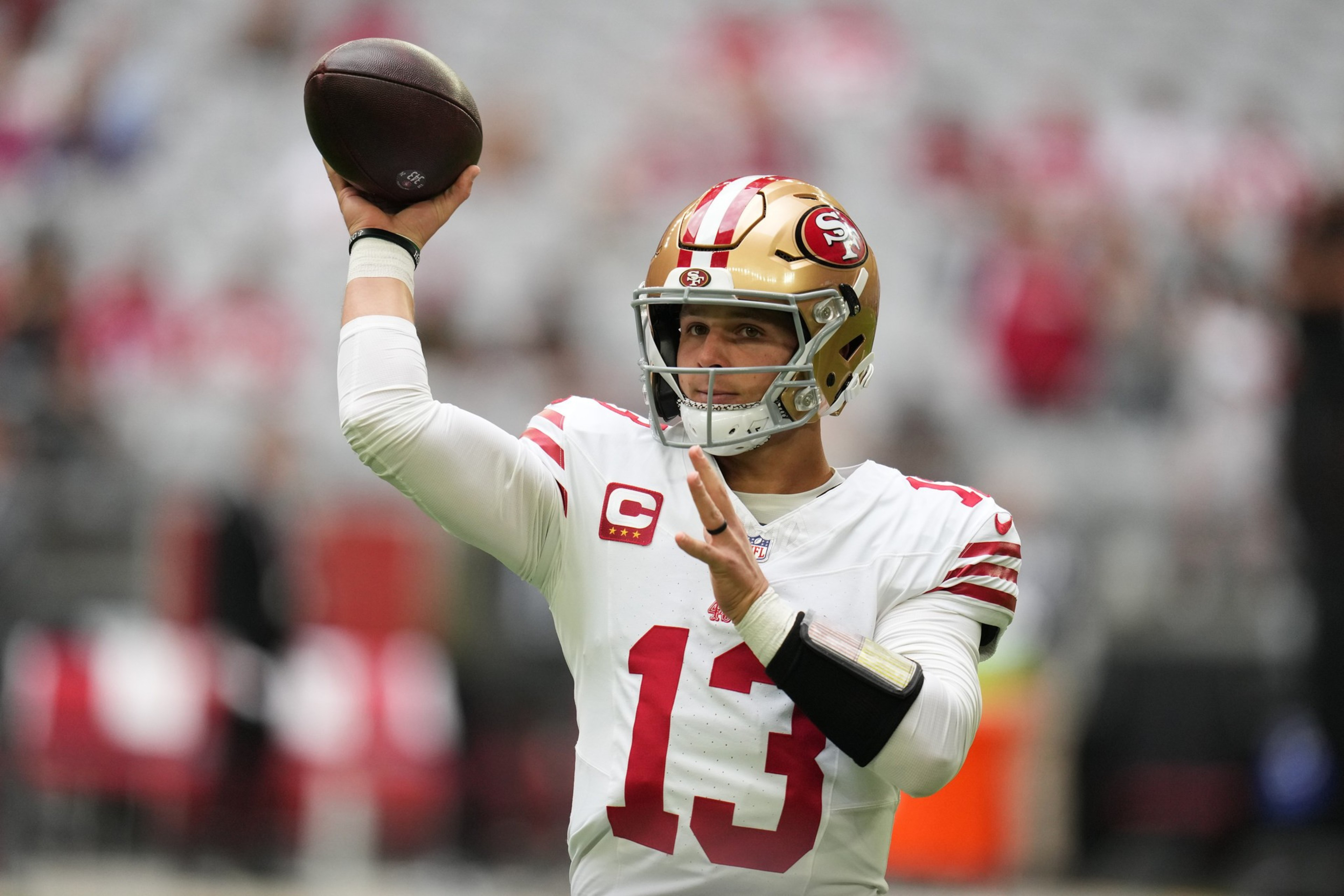 A football player in a white San Francisco 49ers jersey with number 13 prepares to throw a football during a game.