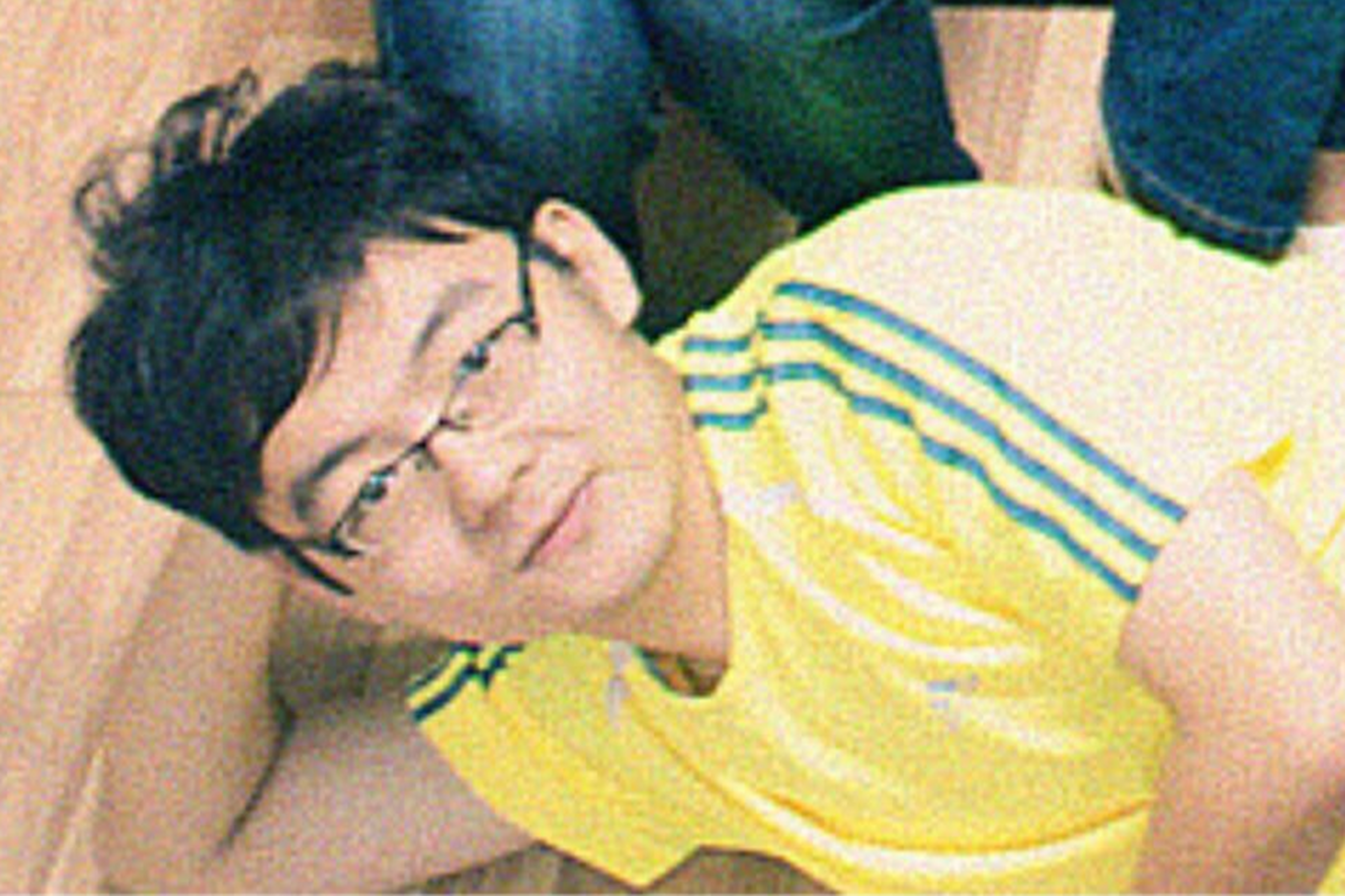 A person with black hair and glasses is lying on the floor wearing a yellow shirt with blue stripes, looking towards the camera.