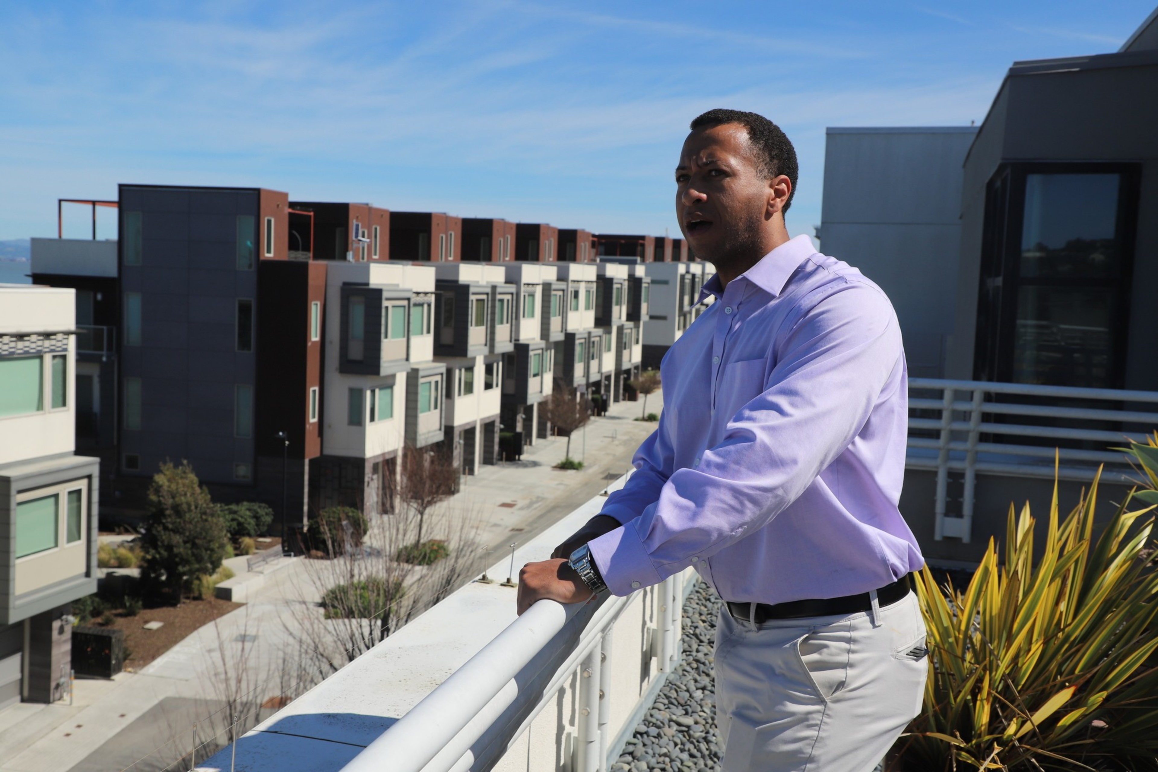 A man leans against the railing of a rooftop deck.