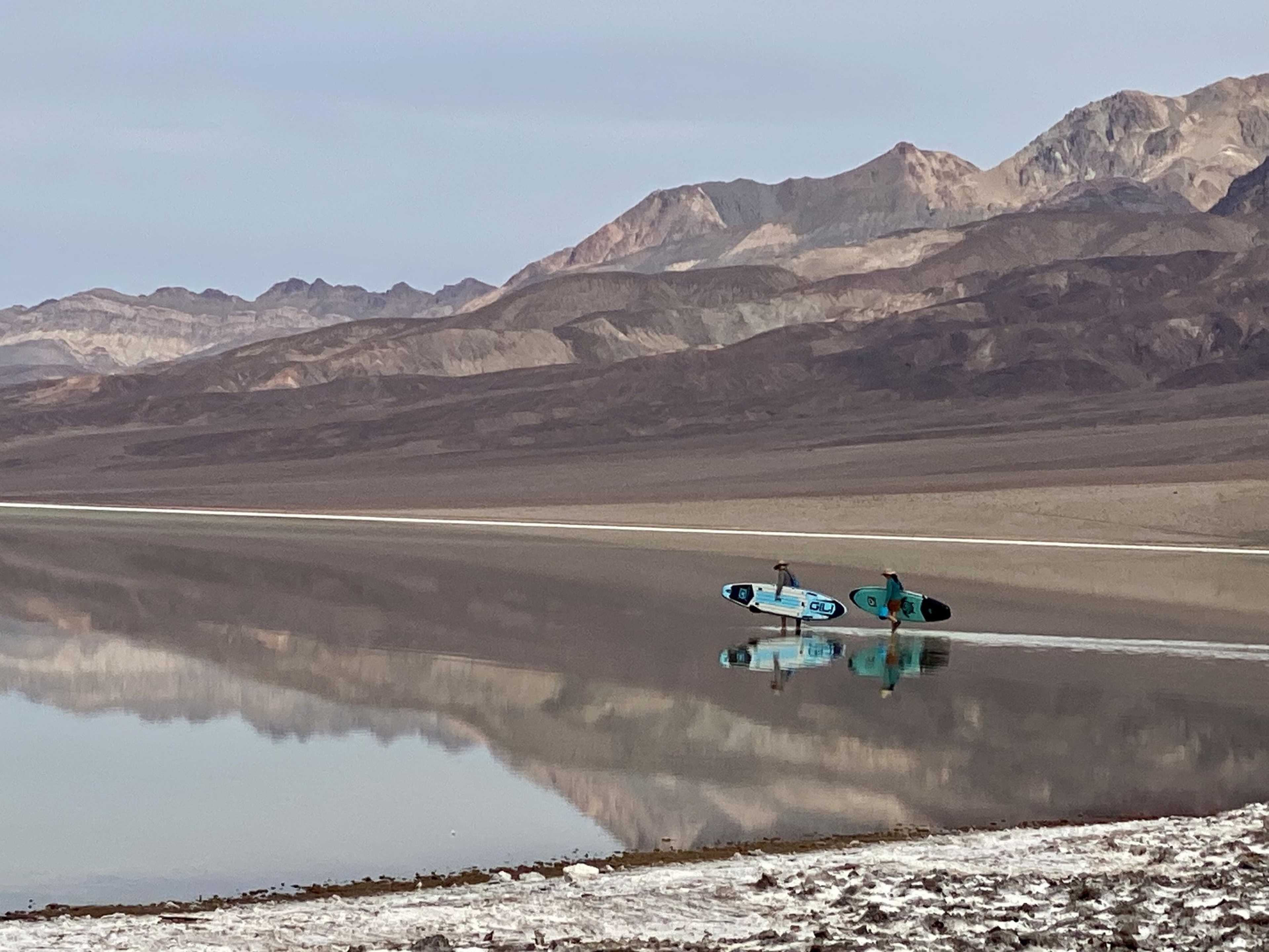 Paddleboarders on the shore of a lake in a desert.
