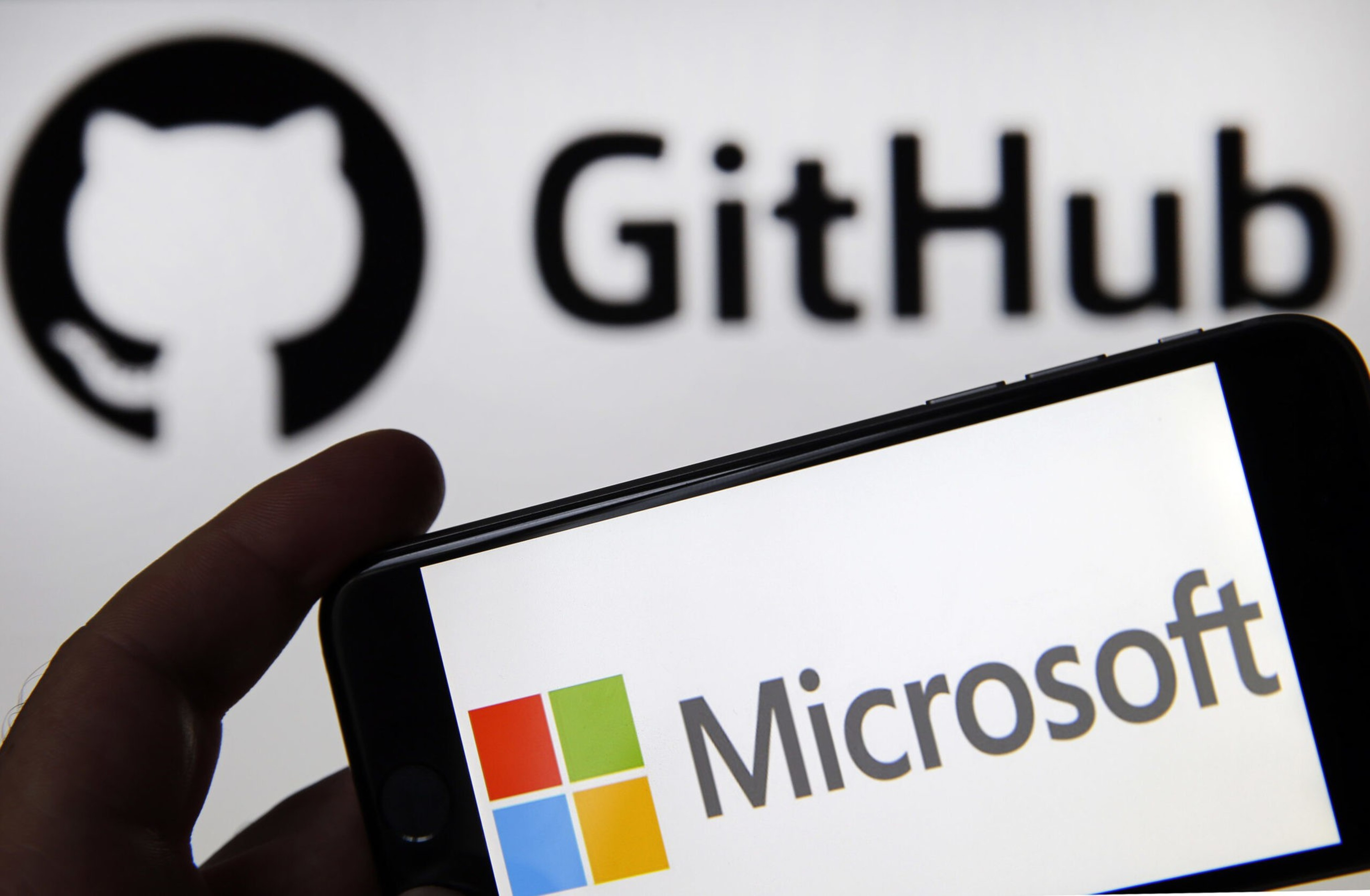 A hand holds a phone displaying the Microsoft logo, with the GitHub logo and text blurred in the background.
