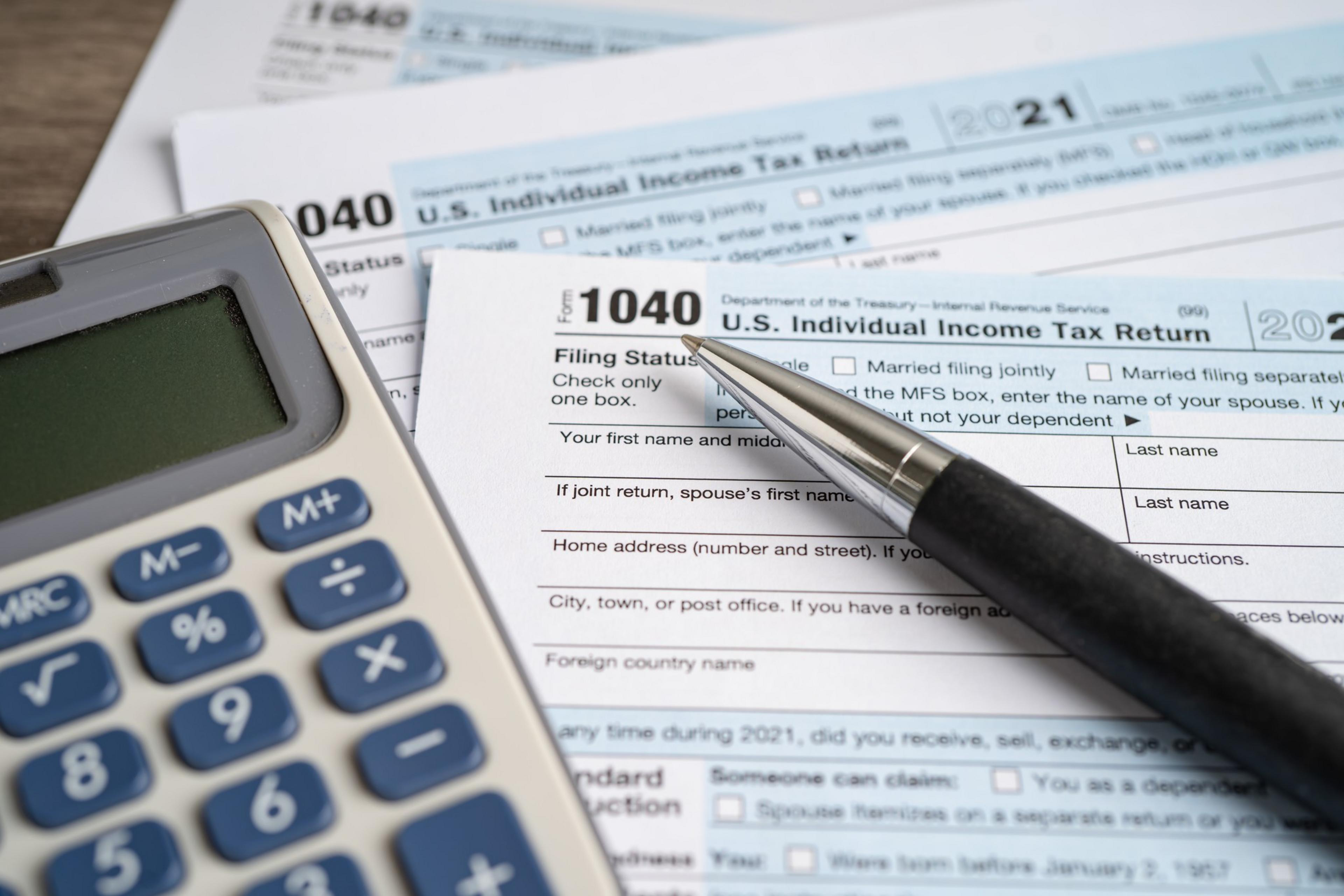 A calculator, pen, and U.S. tax forms for year 2021, suggesting the preparation of an income tax return.