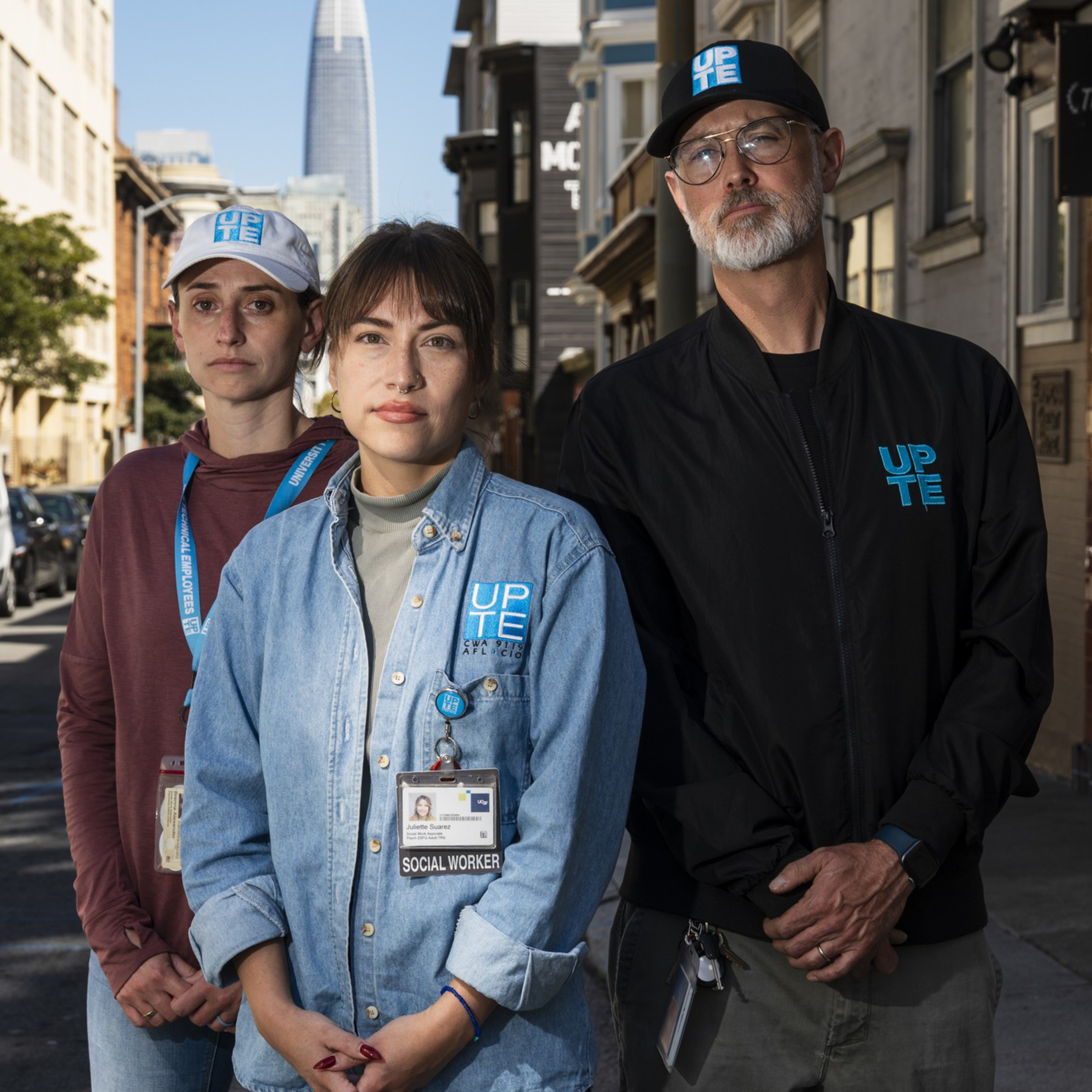 Three people wearing UPT Energy clothing stand confidently on a city street, with a tall skyscraper visible in the background.