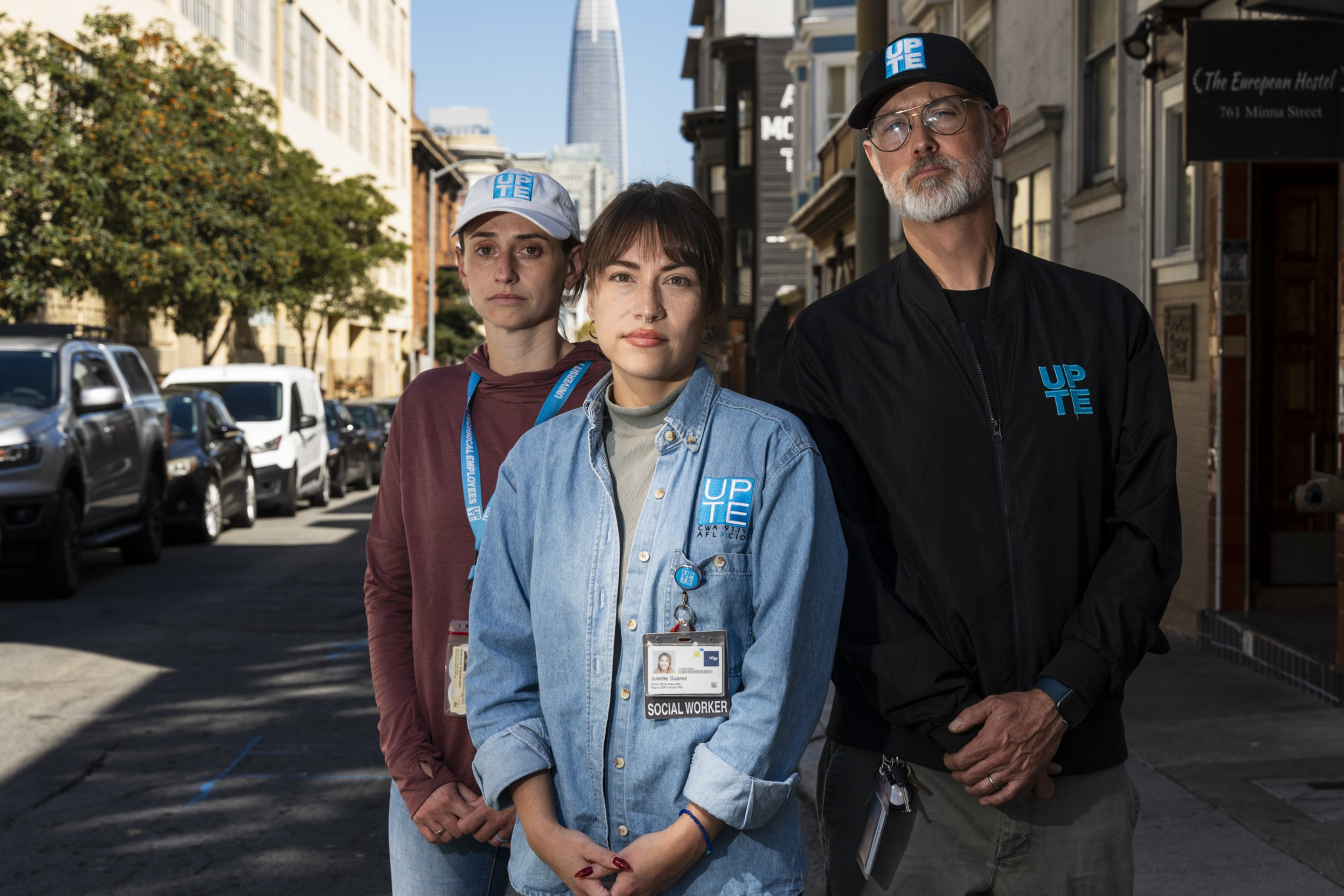Three people wearing UPT Energy clothing stand confidently on a city street, with a tall skyscraper visible in the background.