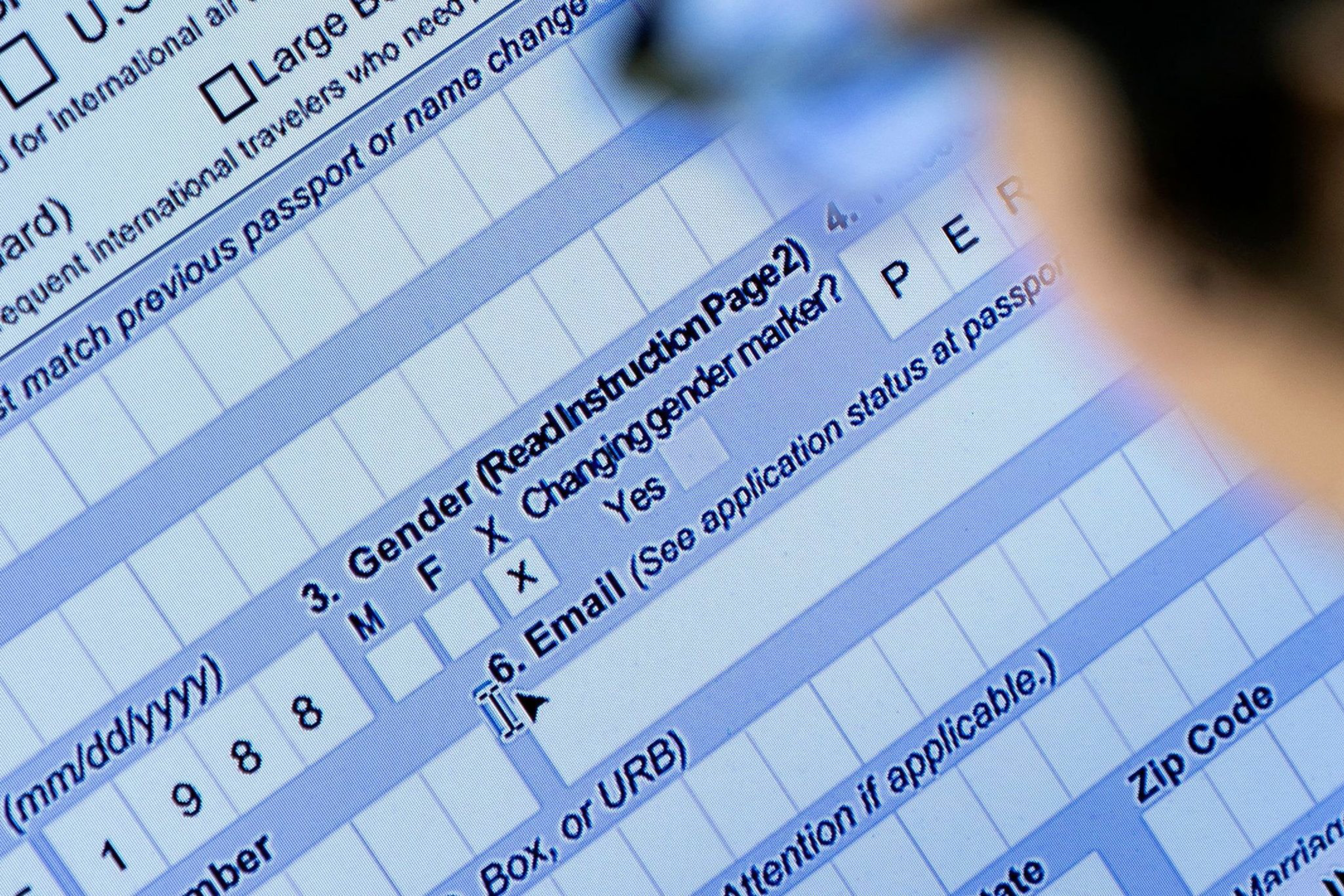 The image shows a close-up of a digital form on a screen, highlighting sections for gender, email, and personal details. A person is looking at the screen.