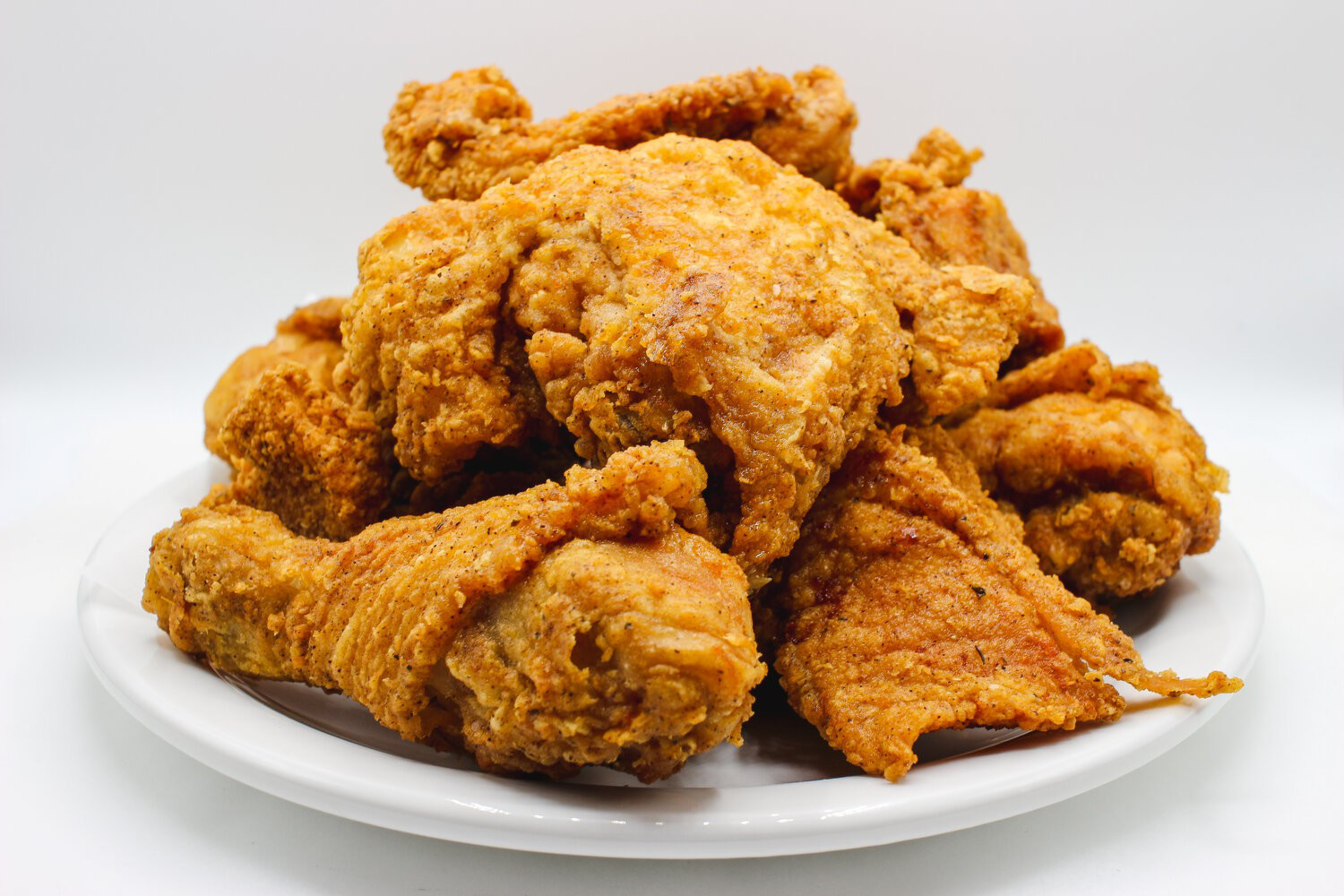 A white plate piled high with golden-brown, crispy fried chicken pieces, including drumsticks and thighs.