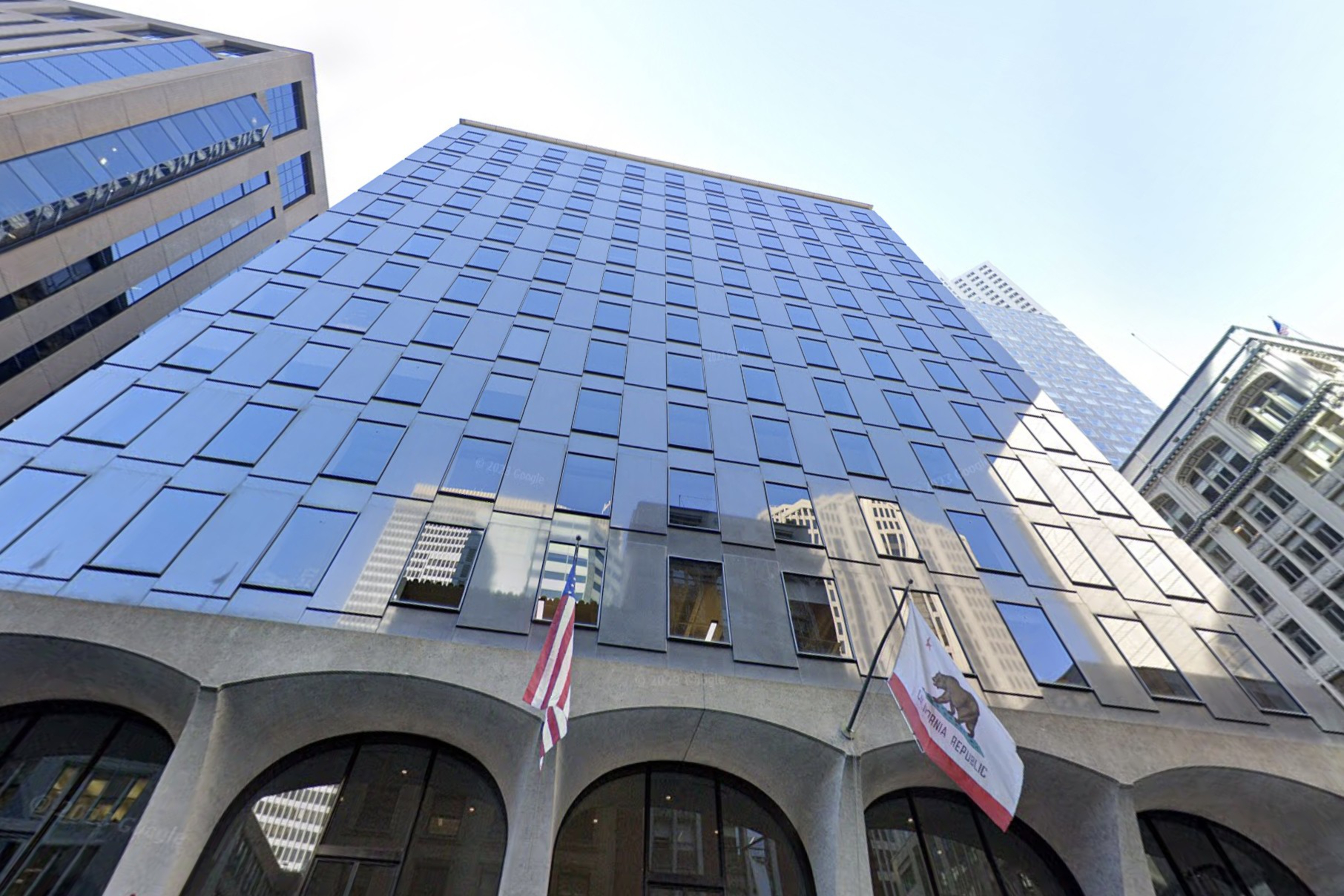 A modern high-rise building with a reflective blue glass facade and arch-shaped concrete entrance, flanked by American and corporate flags.
