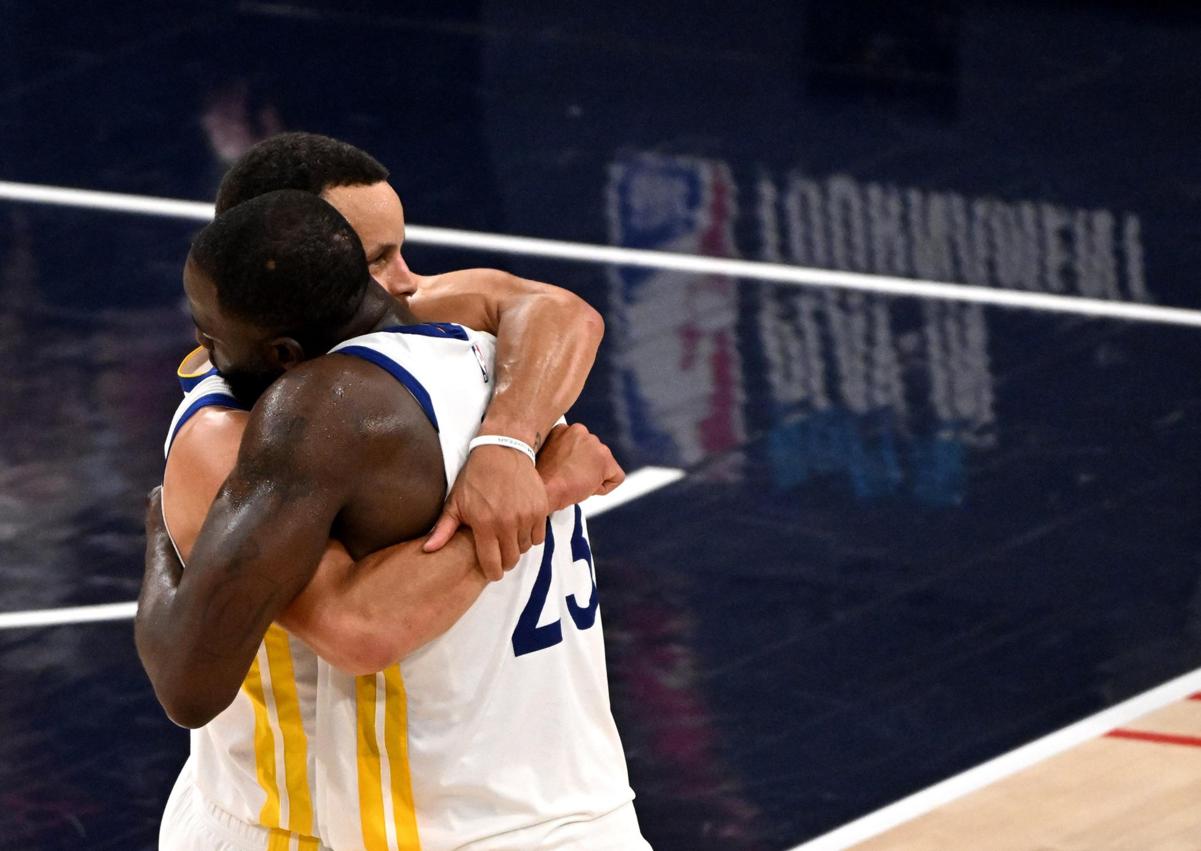 Two basketball players in white and yellow uniforms embrace tightly on the court, showing a moment of celebration or support.