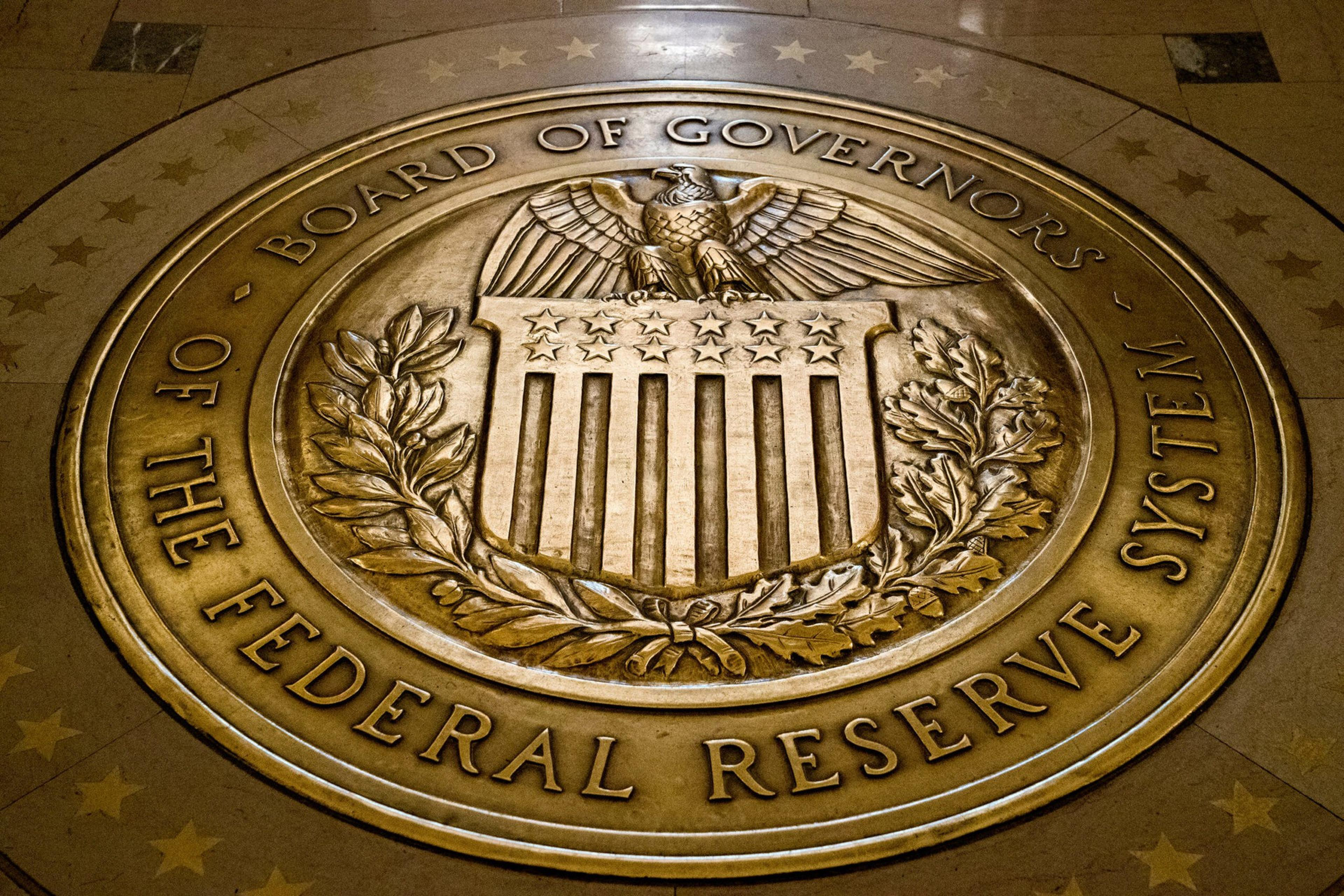 A bronze seal of the Board of Governors of the Federal Reserve System features an eagle above a shield with stars and stripes, surrounded by a laurel wreath.