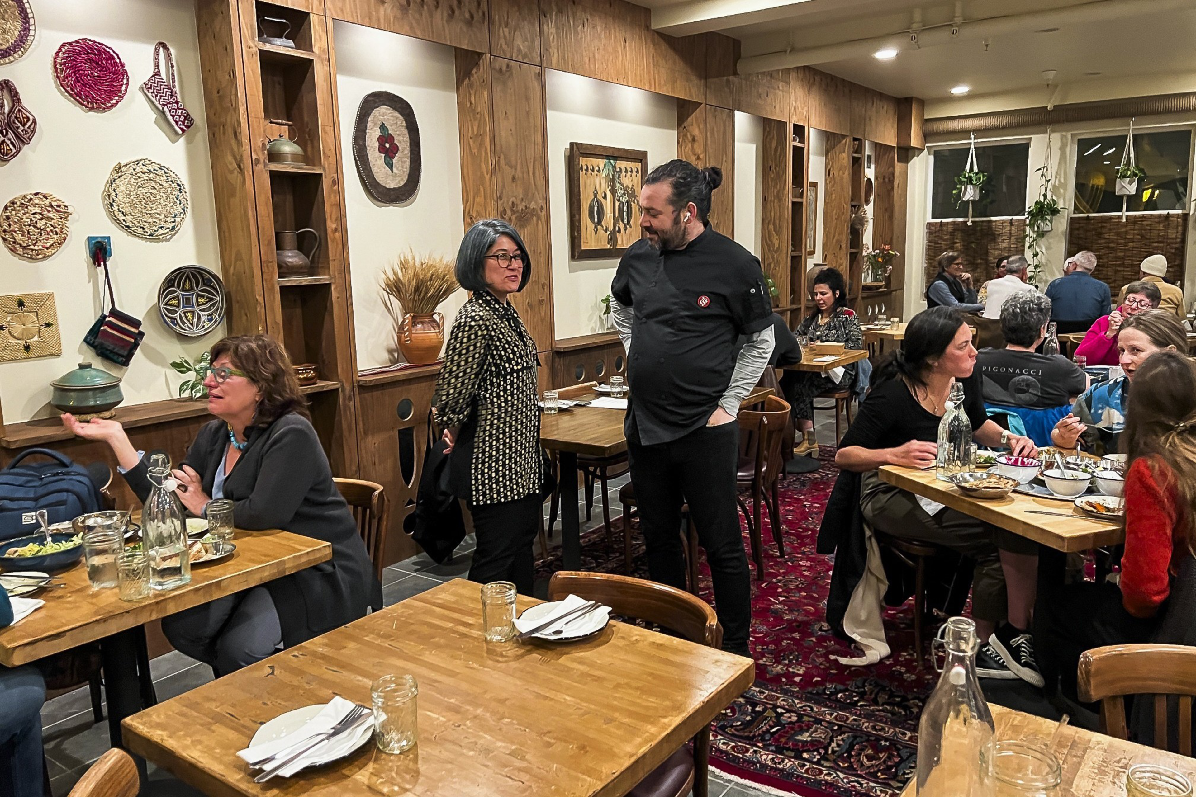 A bustling restaurant interior with diners at wooden tables and rustic decor on the walls.