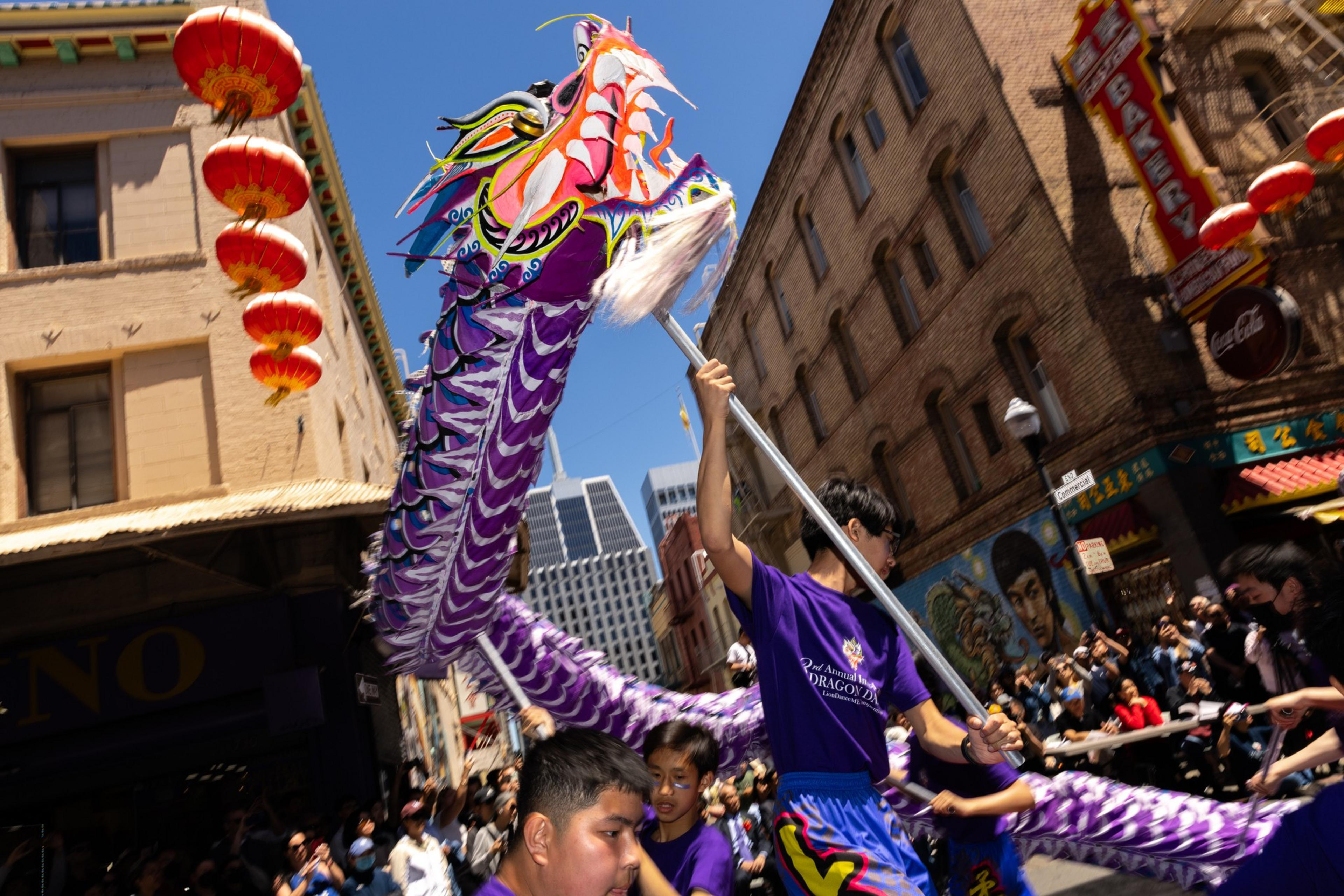 A vibrant dragon dance in a street parade with onlookers and red lanterns.