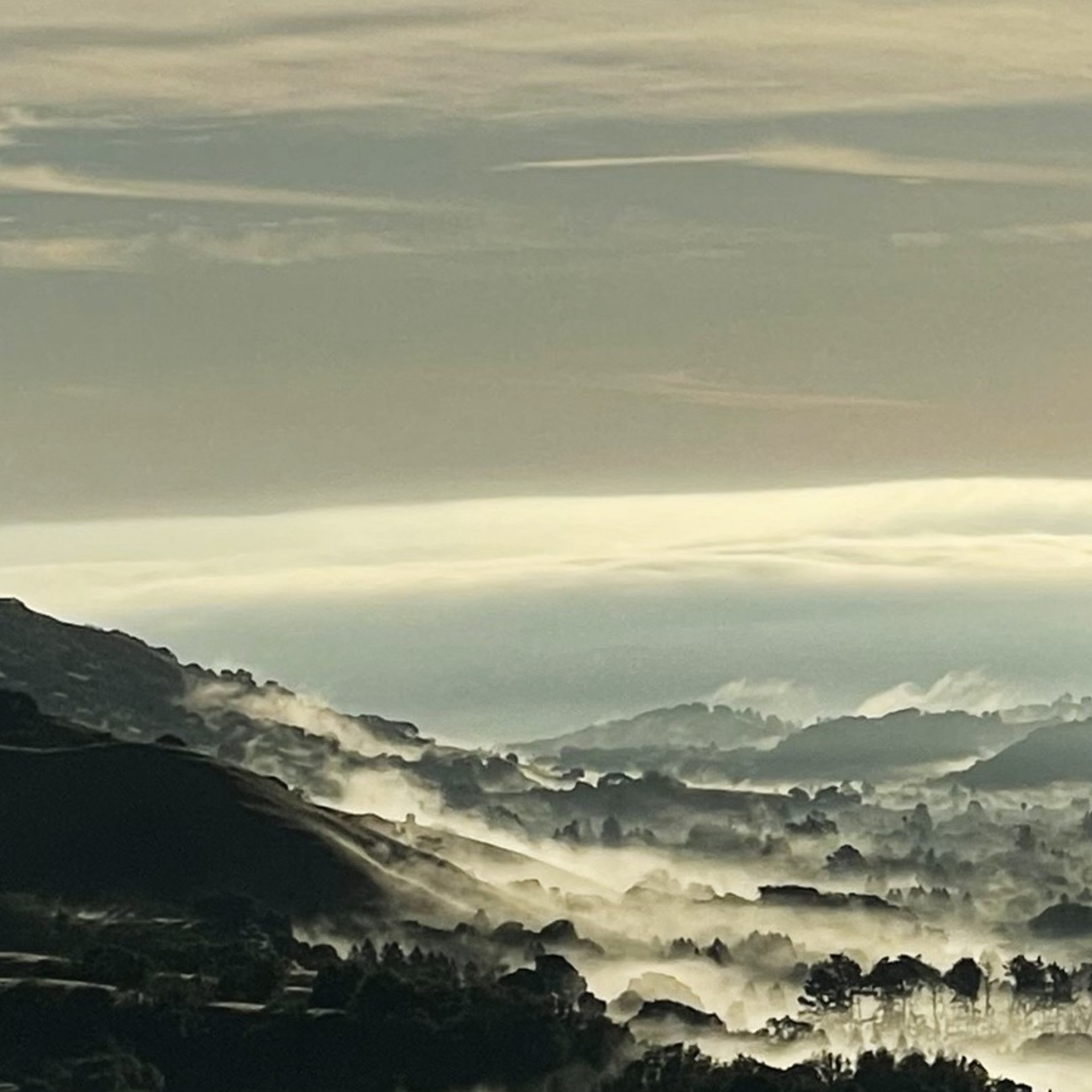 A scenic view of valleys shrouded in mist with rolling hills and a winding road in the foreground, featuring a yellow road sign with a right turn arrow.