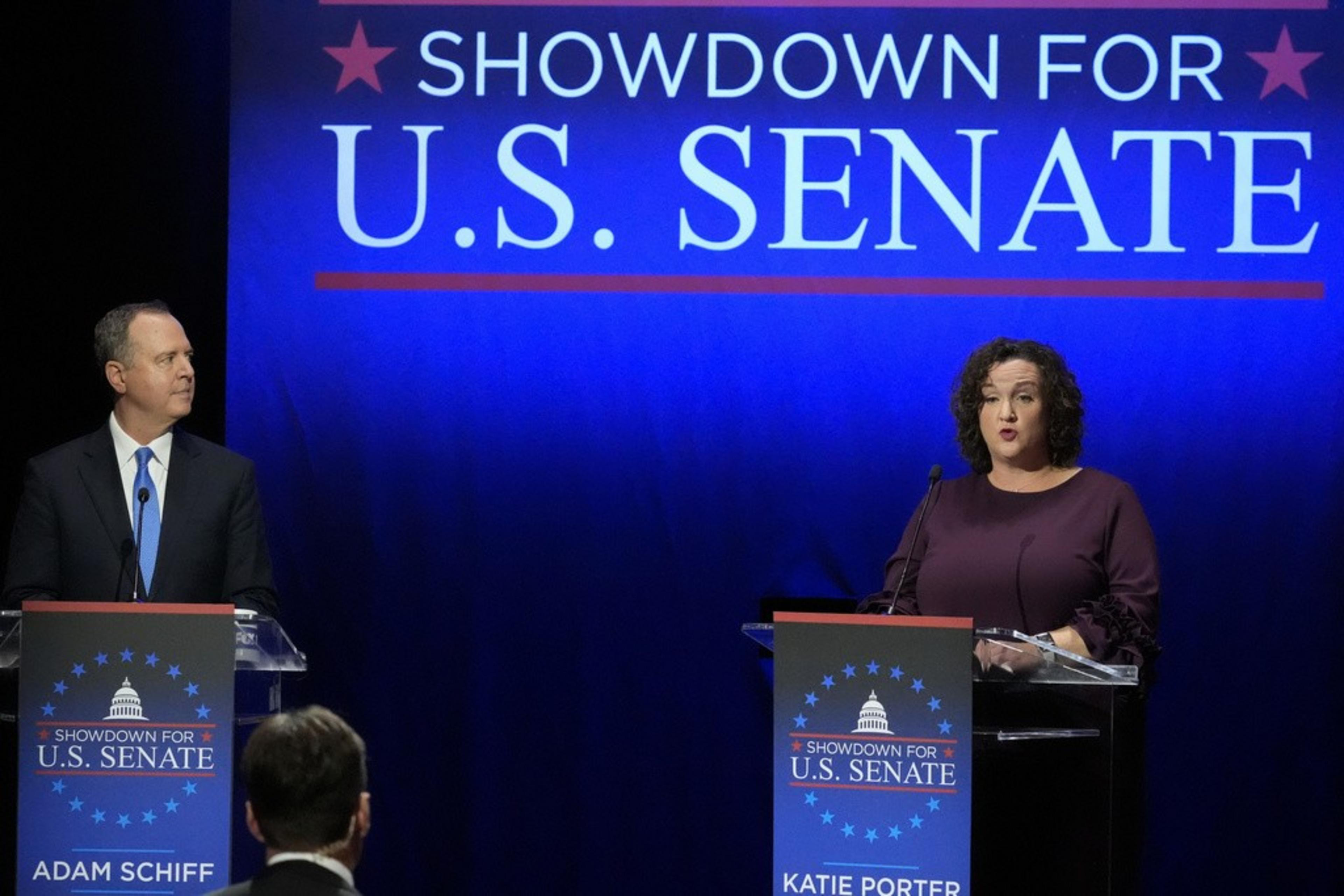 Two individuals at podiums under a "SHOWDOWN FOR U.S. SENATE" sign, engaged in what appears to be a political debate.
