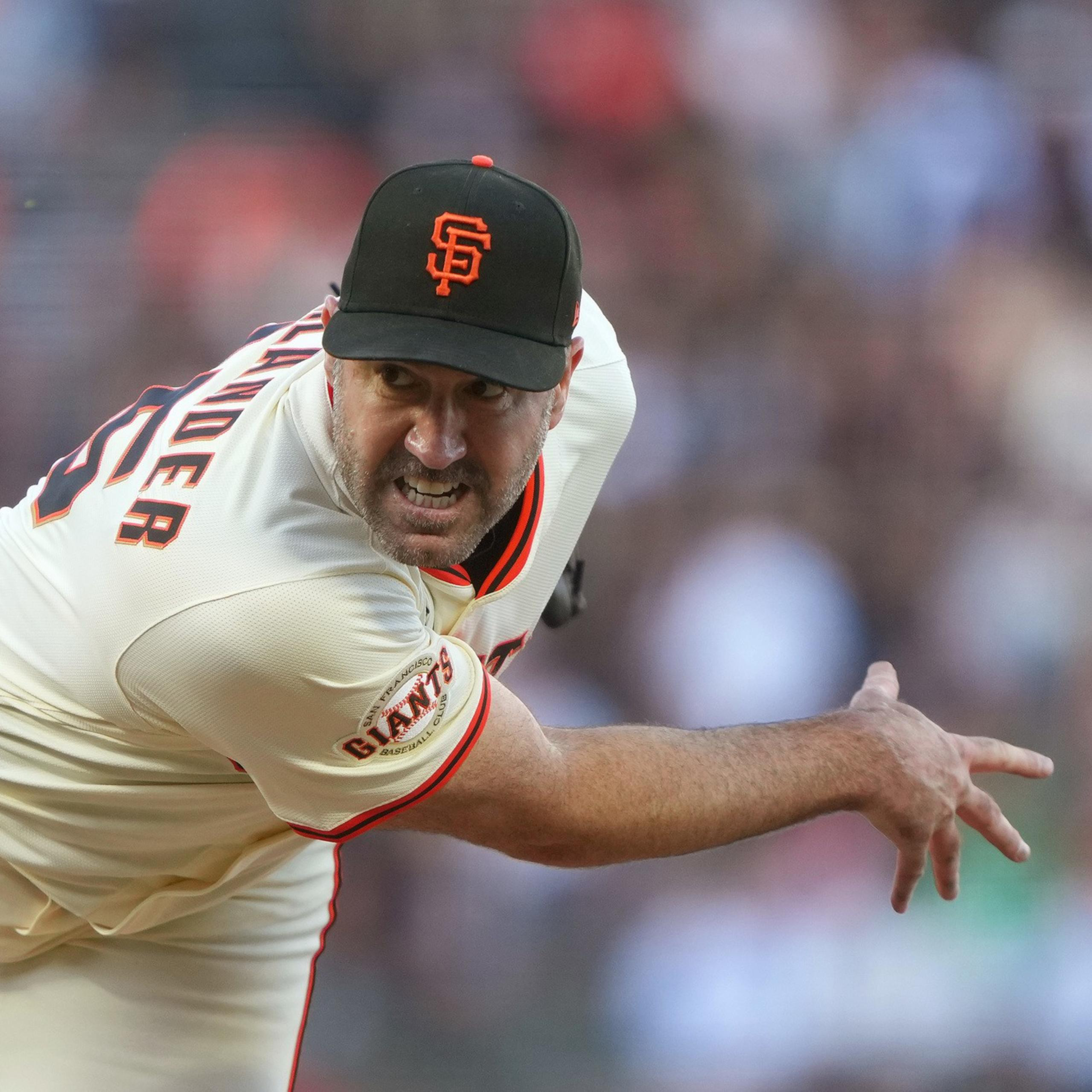 A baseball pitcher in a San Francisco Giants uniform is mid-pitch, leaning forward with intense focus and a raised leg, ready to throw the ball.