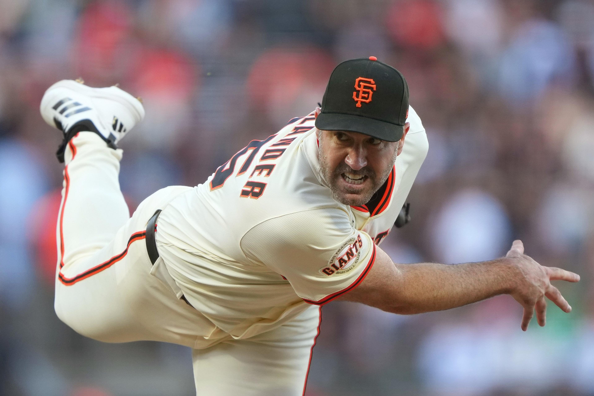 A baseball pitcher in a San Francisco Giants uniform is mid-pitch, leaning forward with intense focus and a raised leg, ready to throw the ball.