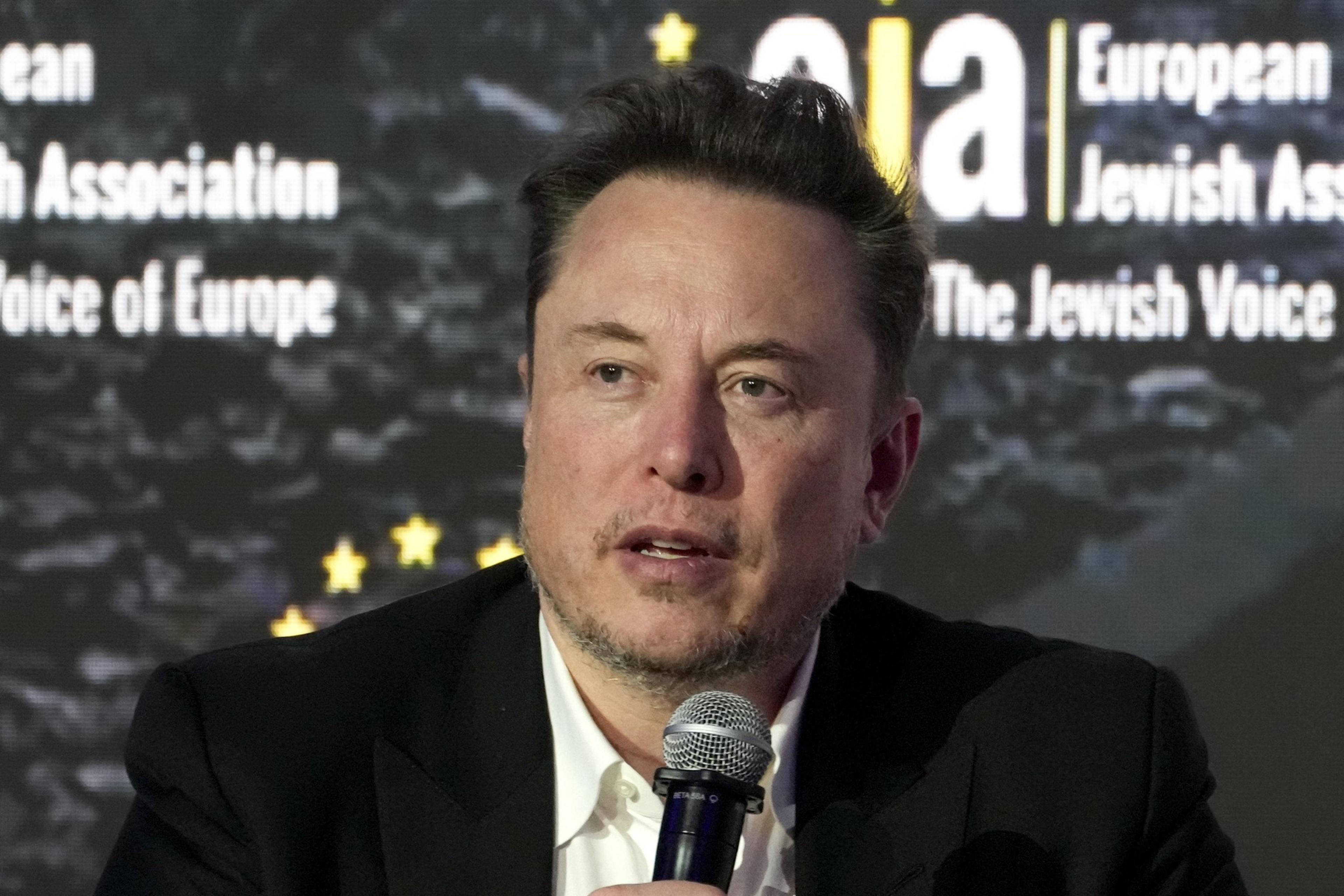 A man speaks into a microphone against a backdrop with text and stars.