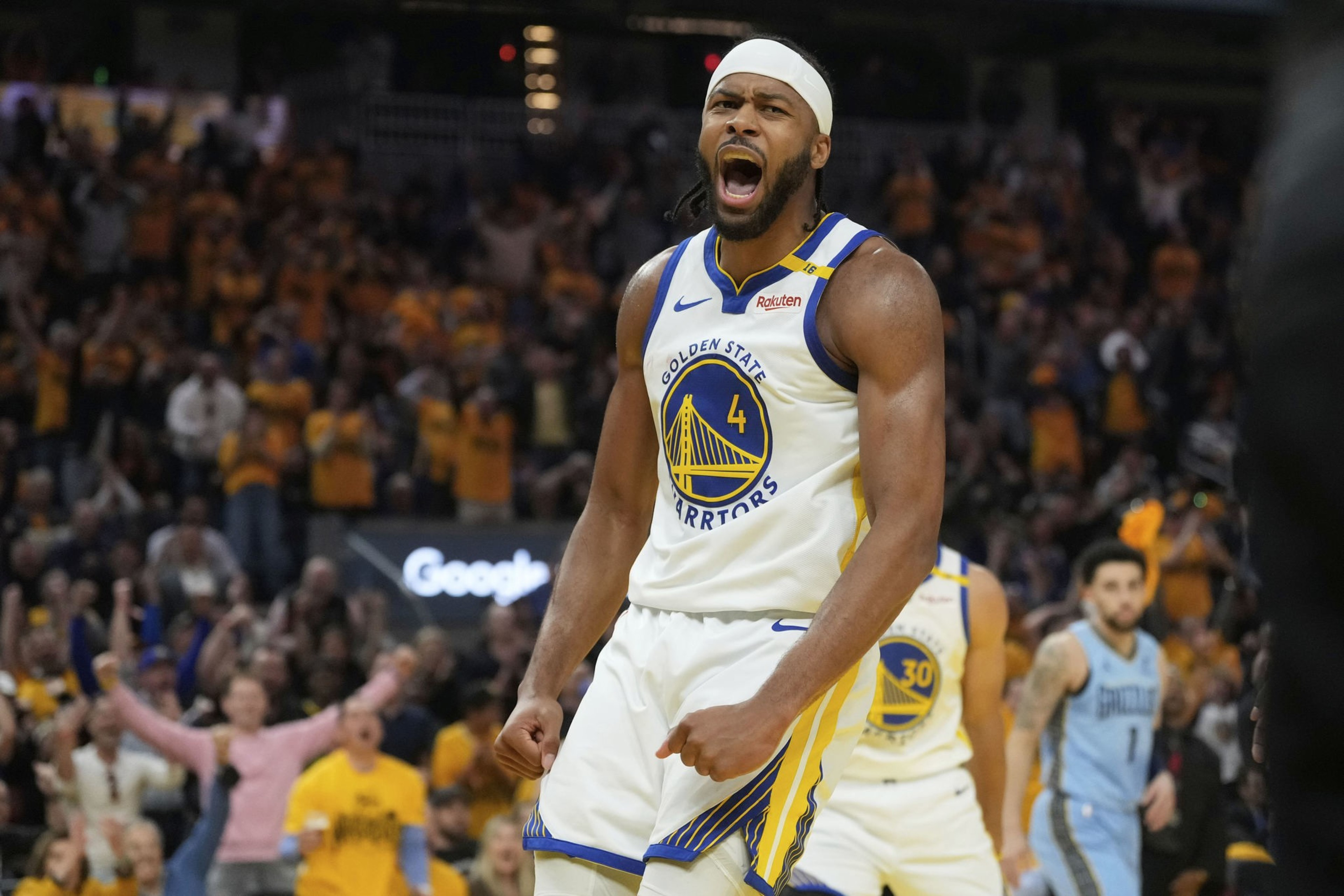 A basketball player in a Golden State Warriors jersey is passionately celebrating on the court, with an excited crowd in the background.