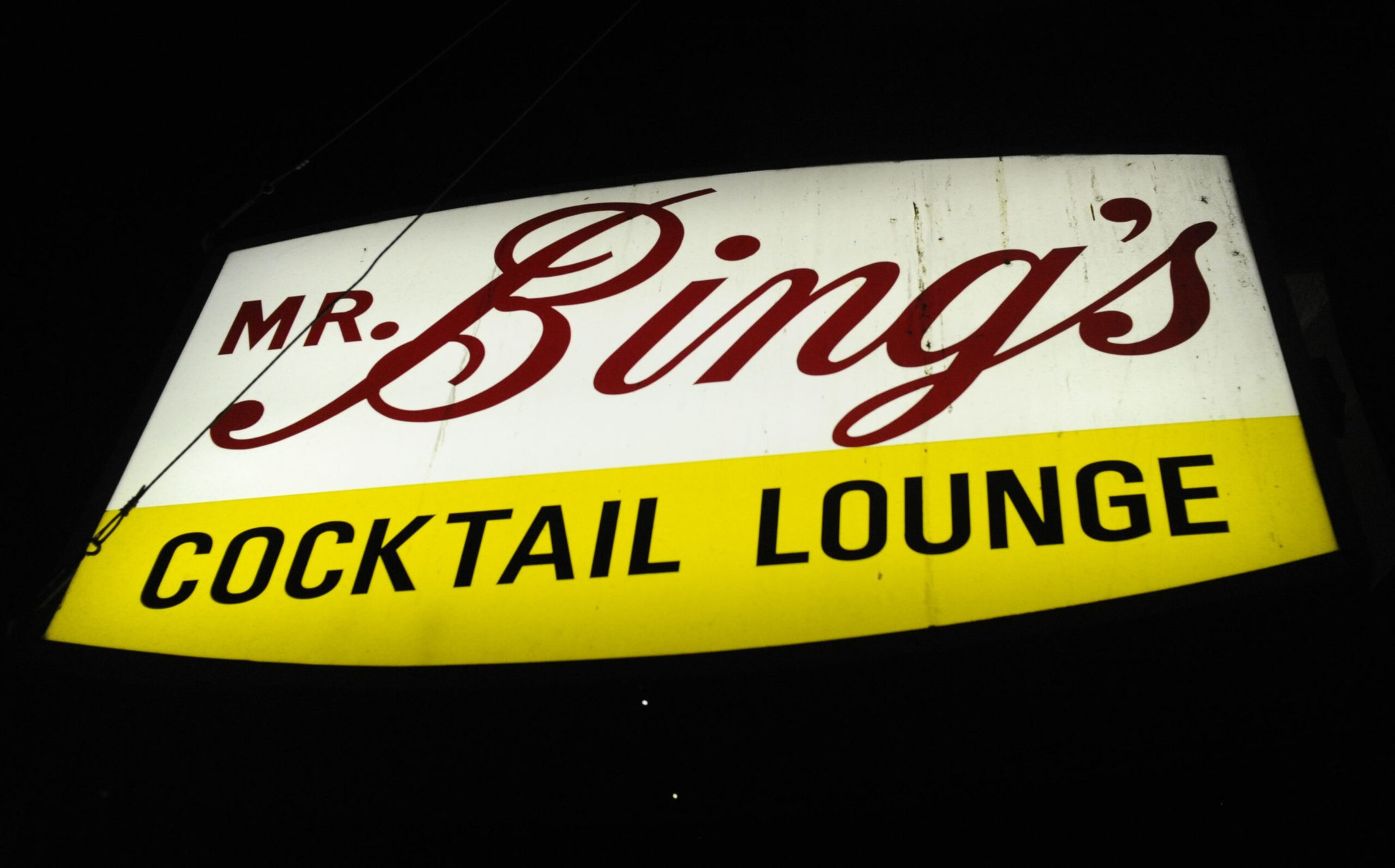 The red and yellow sign of Mr. Bing's Cocktail Lounge features cursive writing. 