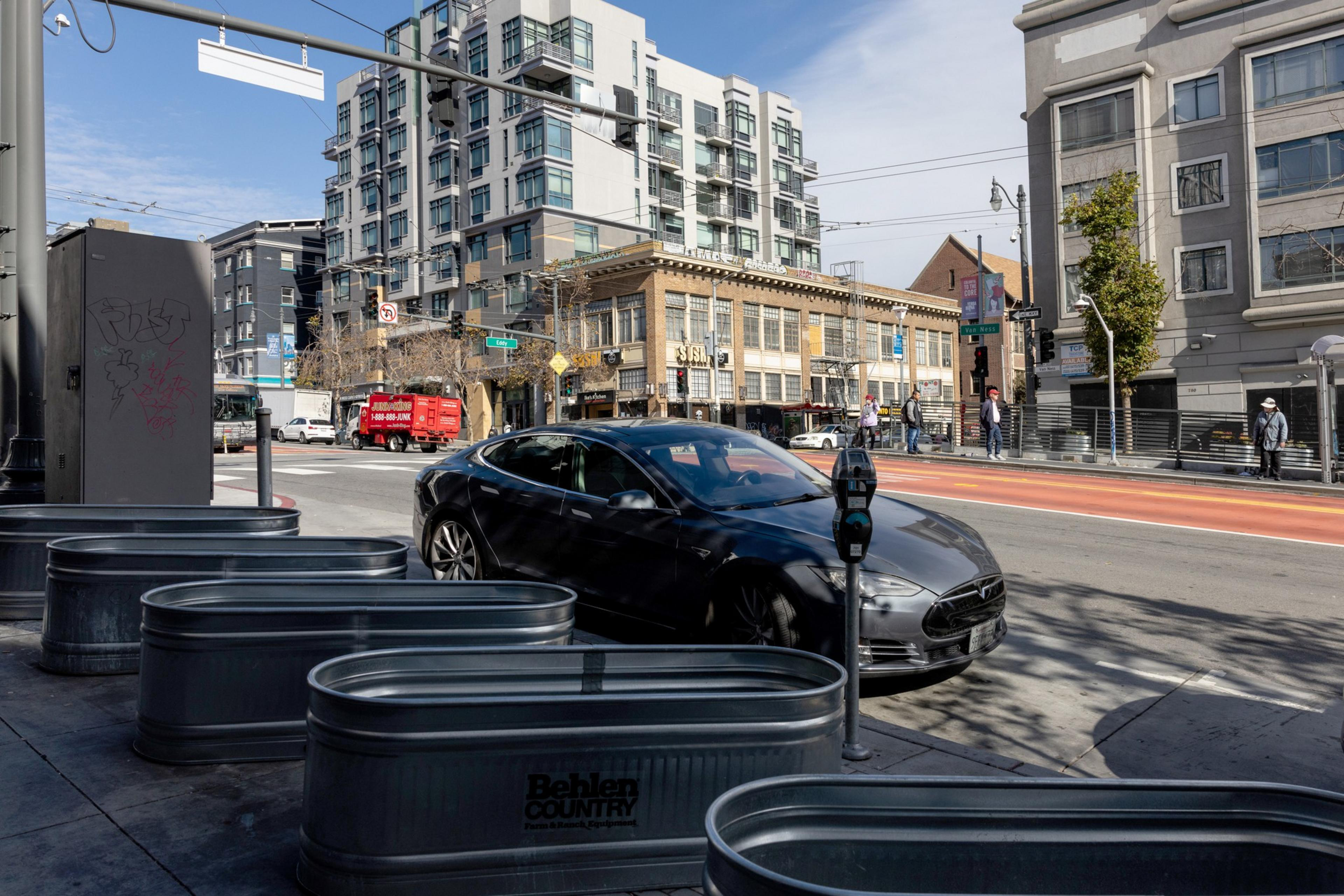 A street scene of tall buildings in the background with oblong planter boxes installed to discourage encampments.