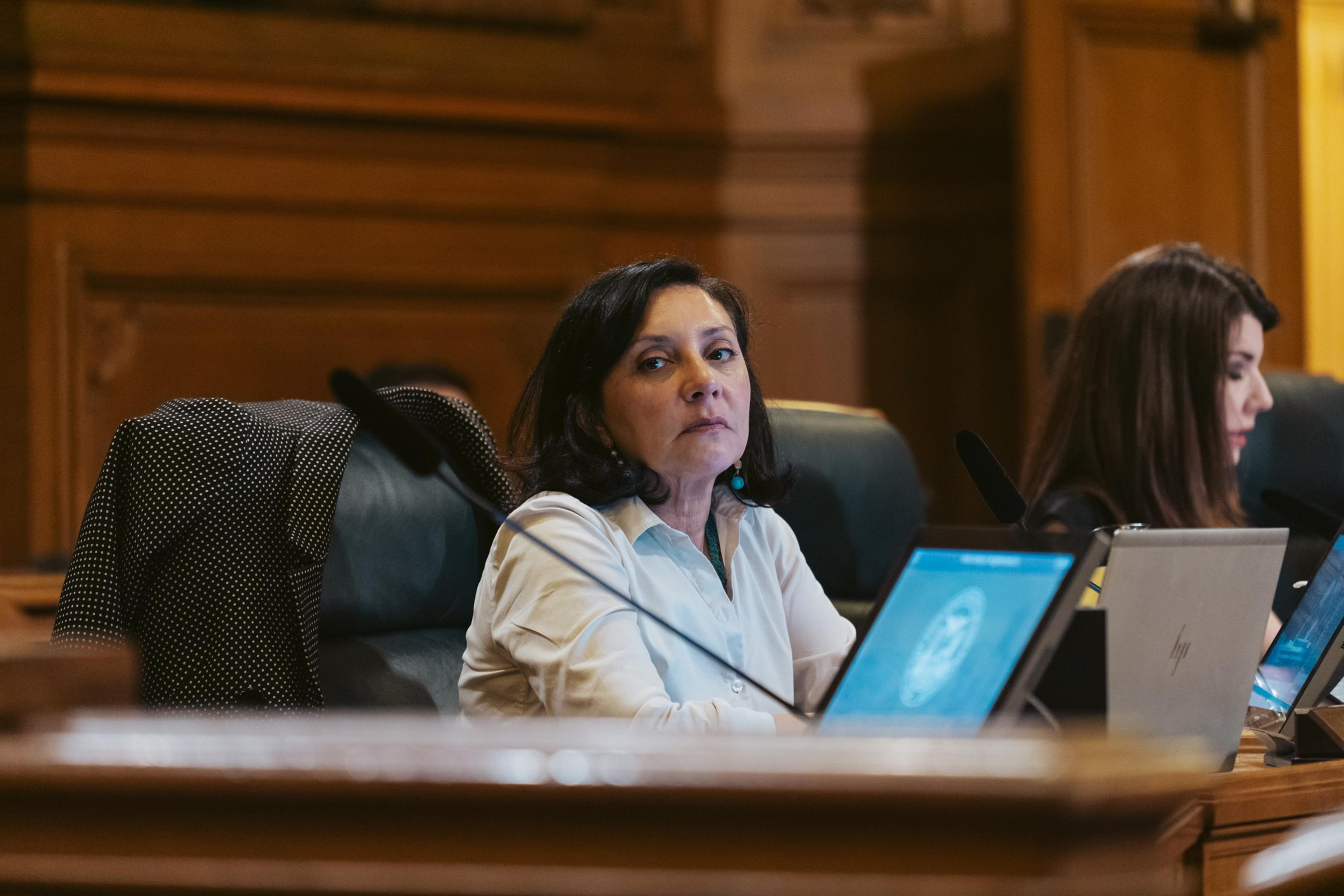 Myrna Melgar cast a serious expression while she sits in front of a laptop and listens intently.