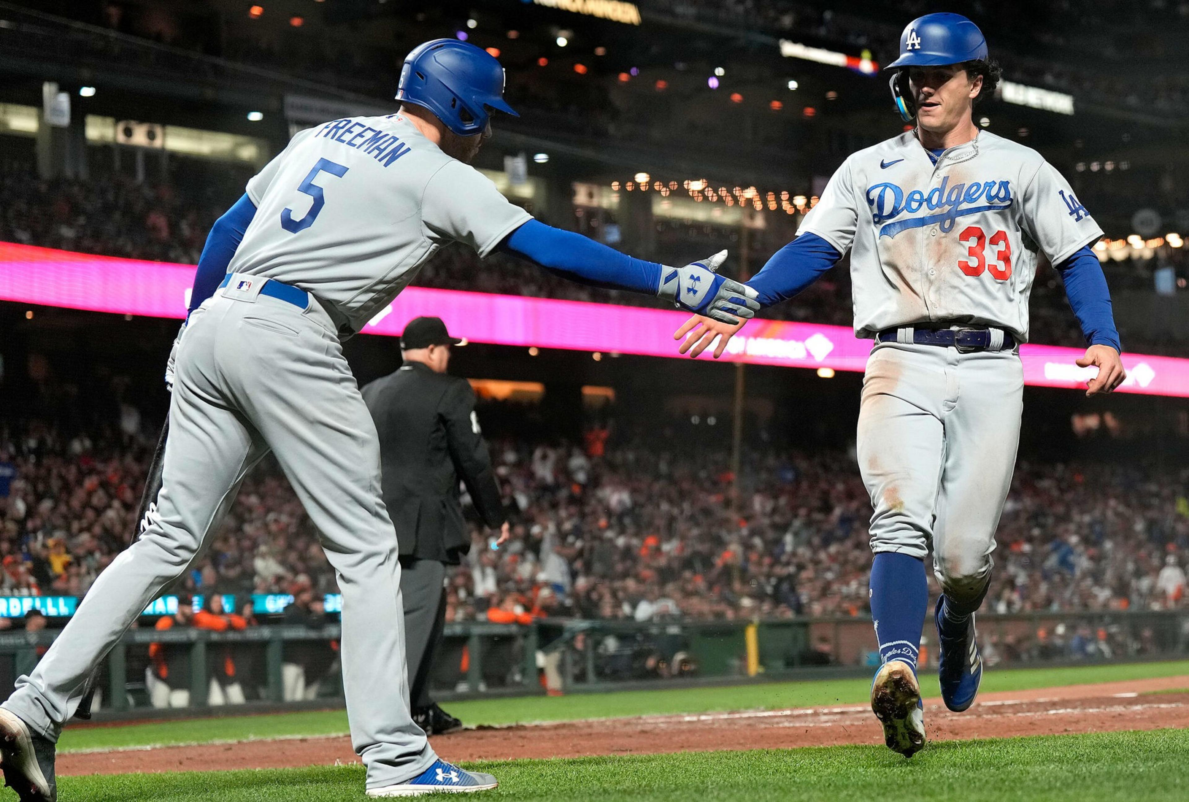 A Dodgers player wearing number 33 high-fives teammate number 5, Freeman, near home plate during a nighttime baseball game.