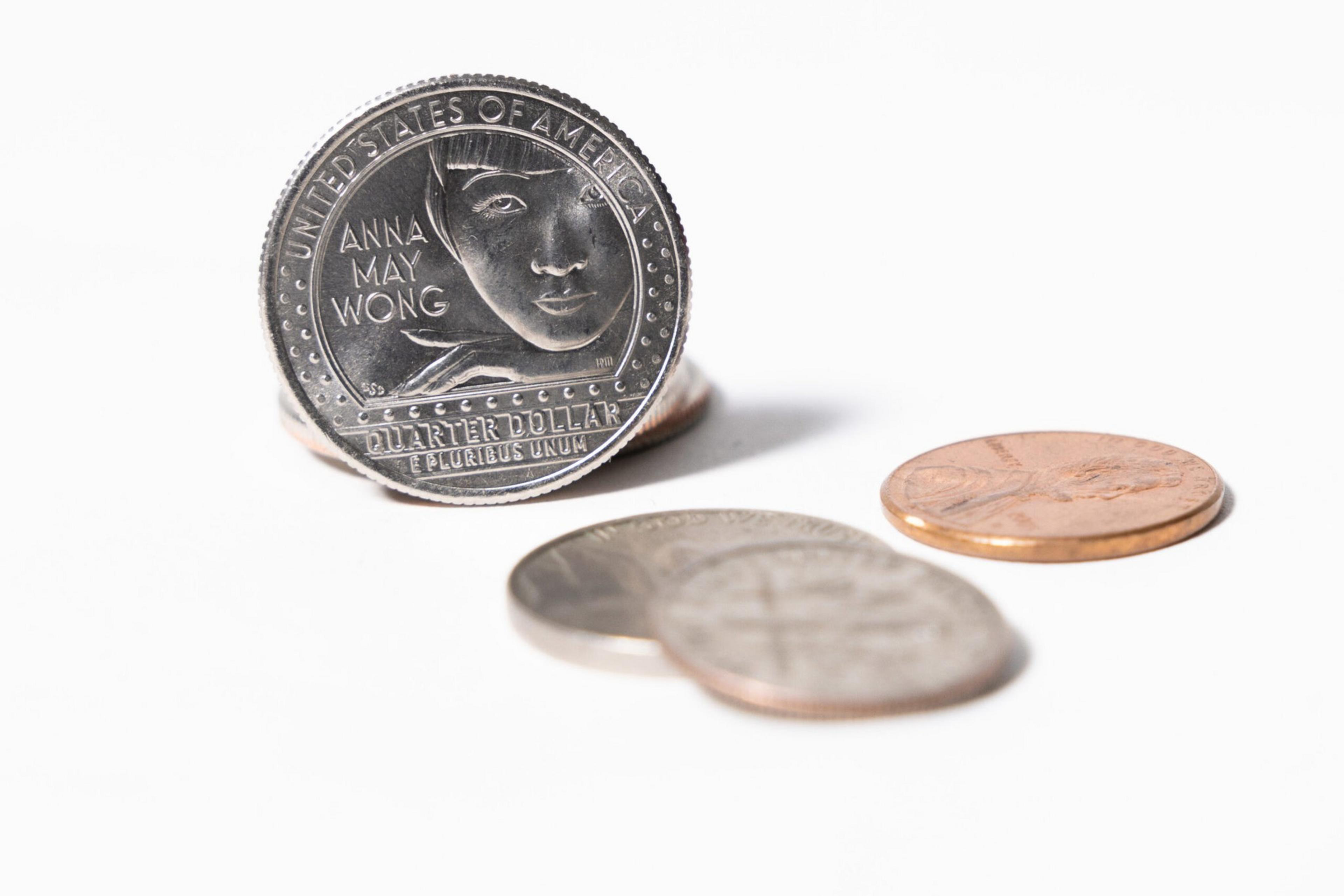 A U.S. quarter featuring Anna May Wong stands upright behind two blurred quarters and a penny on a white surface.