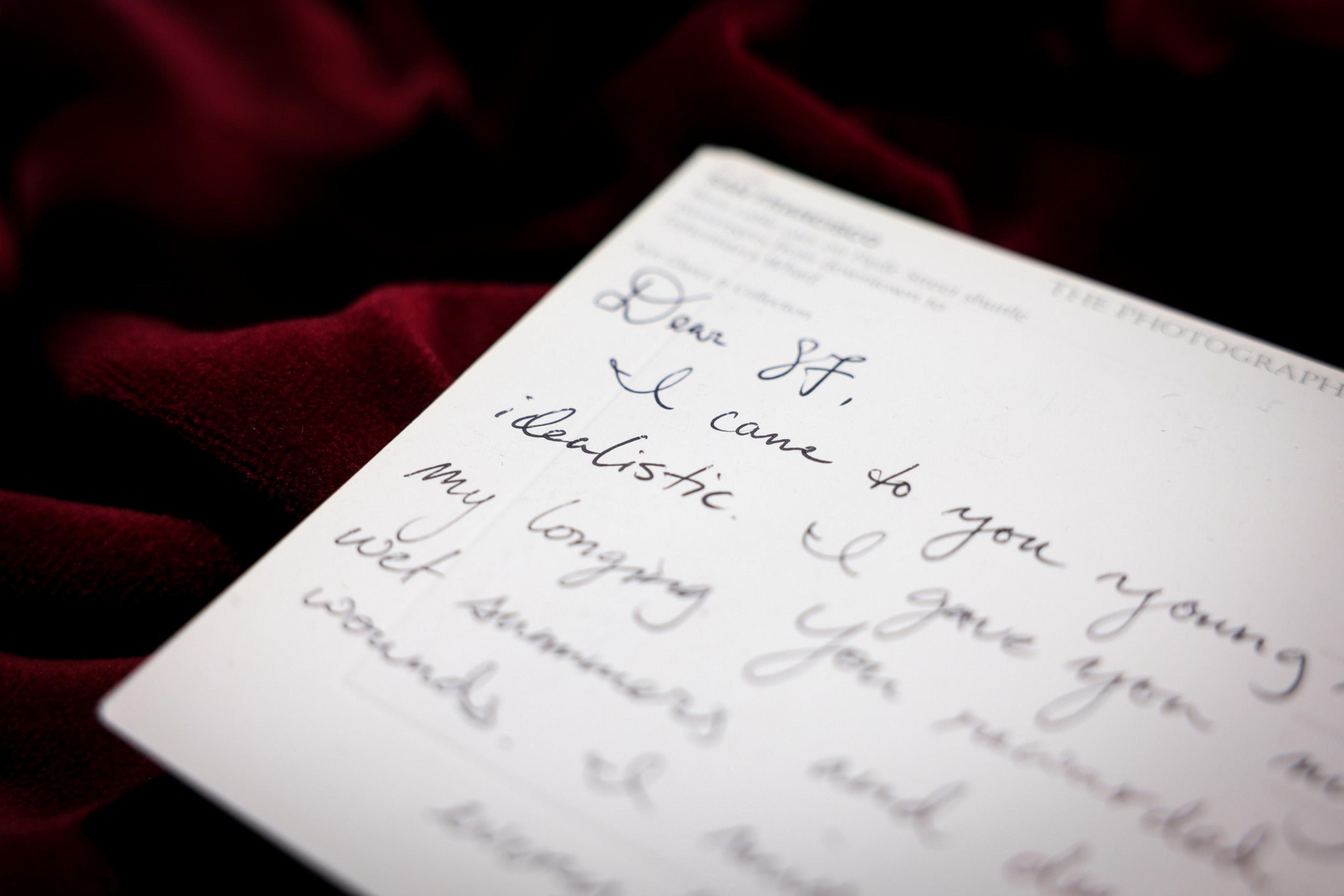 A handwritten letter on white paper lies on dark red fabric, with visible cursive text starting with "Dear St," and mentioning "young" and "realistic."