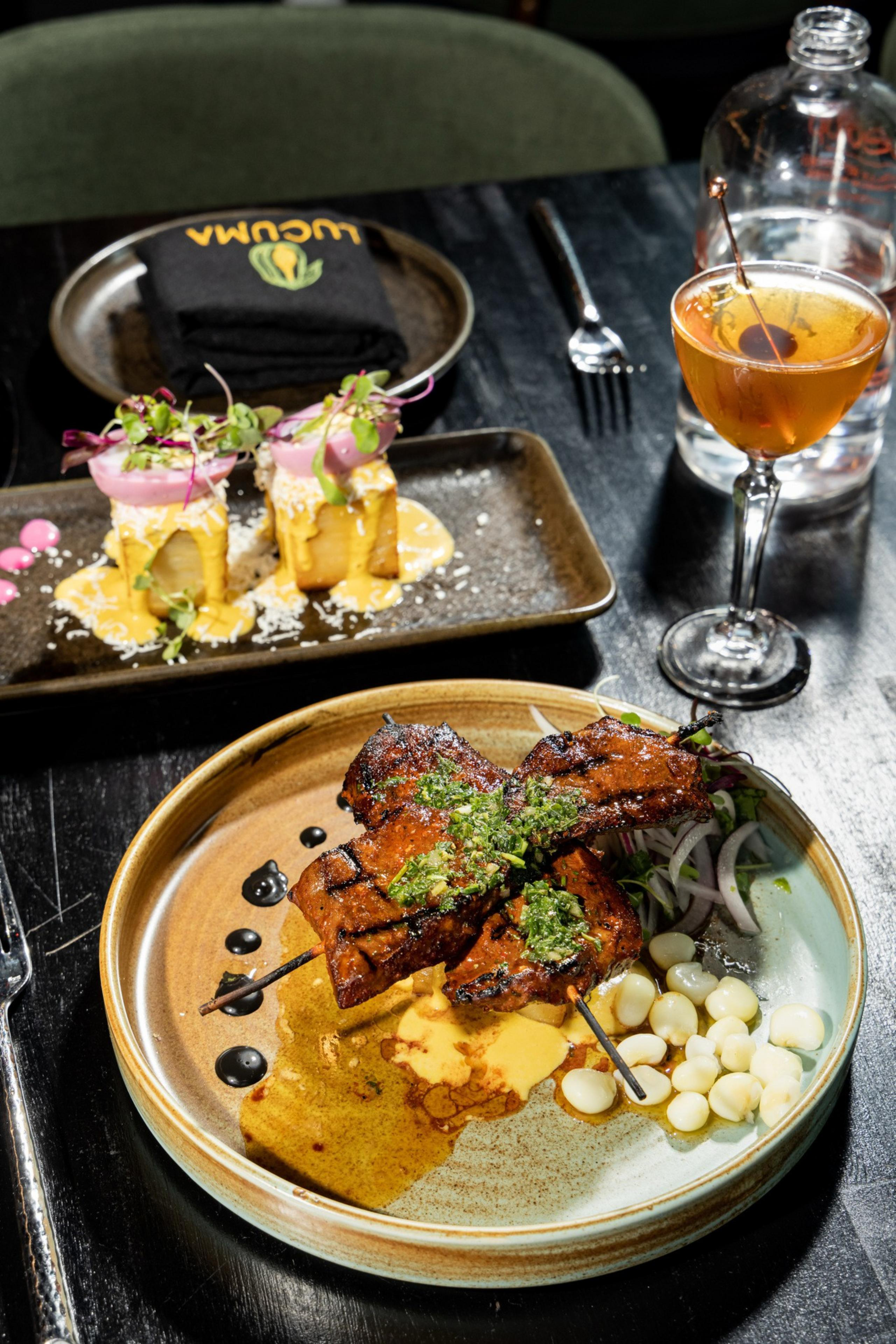 The image shows grilled meat skewers with sauce and corn, a dish with cheese and microgreens, a cocktail with a cherry, and a plate with a folded napkin.