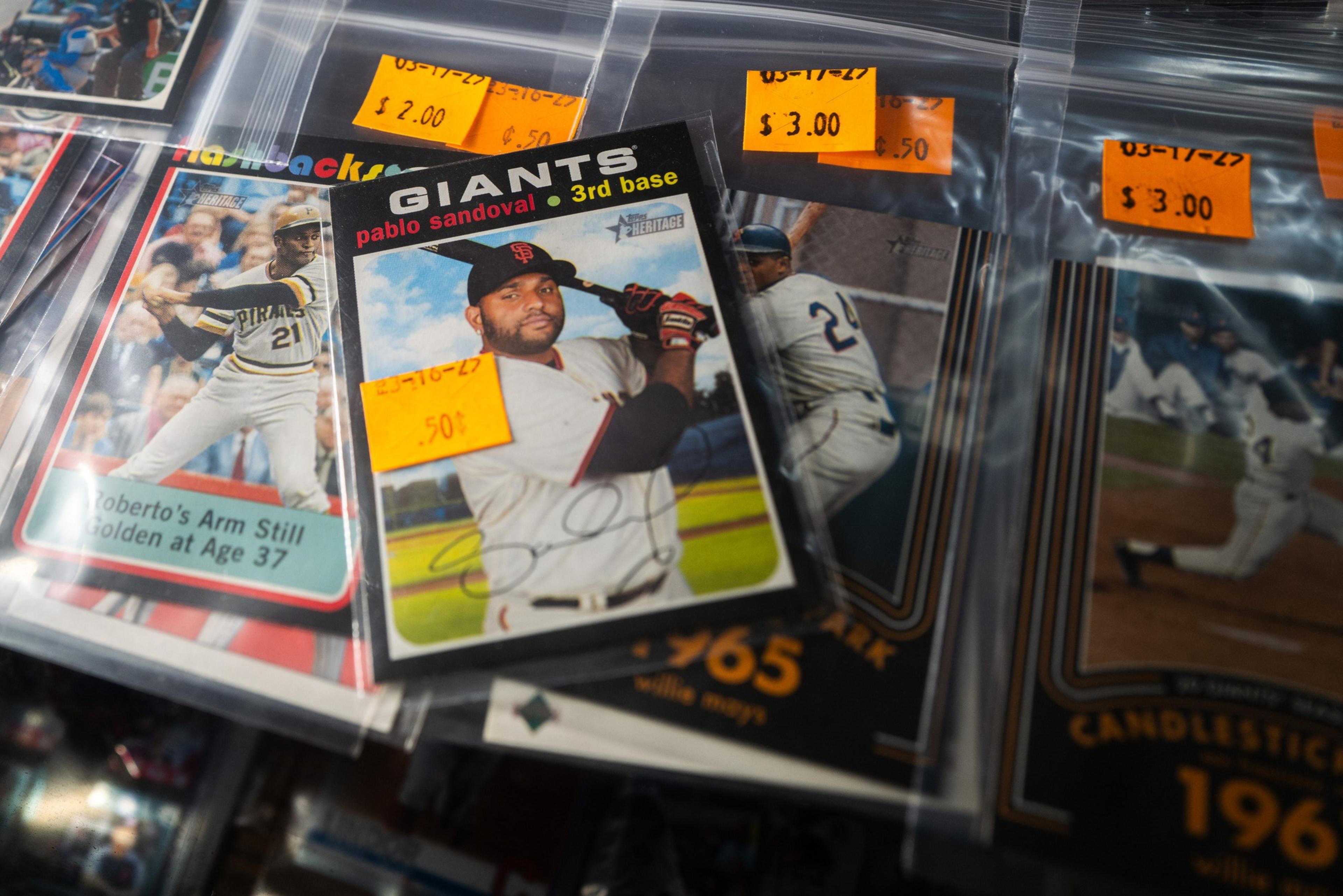 The image shows a collection of baseball cards in plastic sleeves with orange price tags, featuring various players and their names, teams, and playing stats.