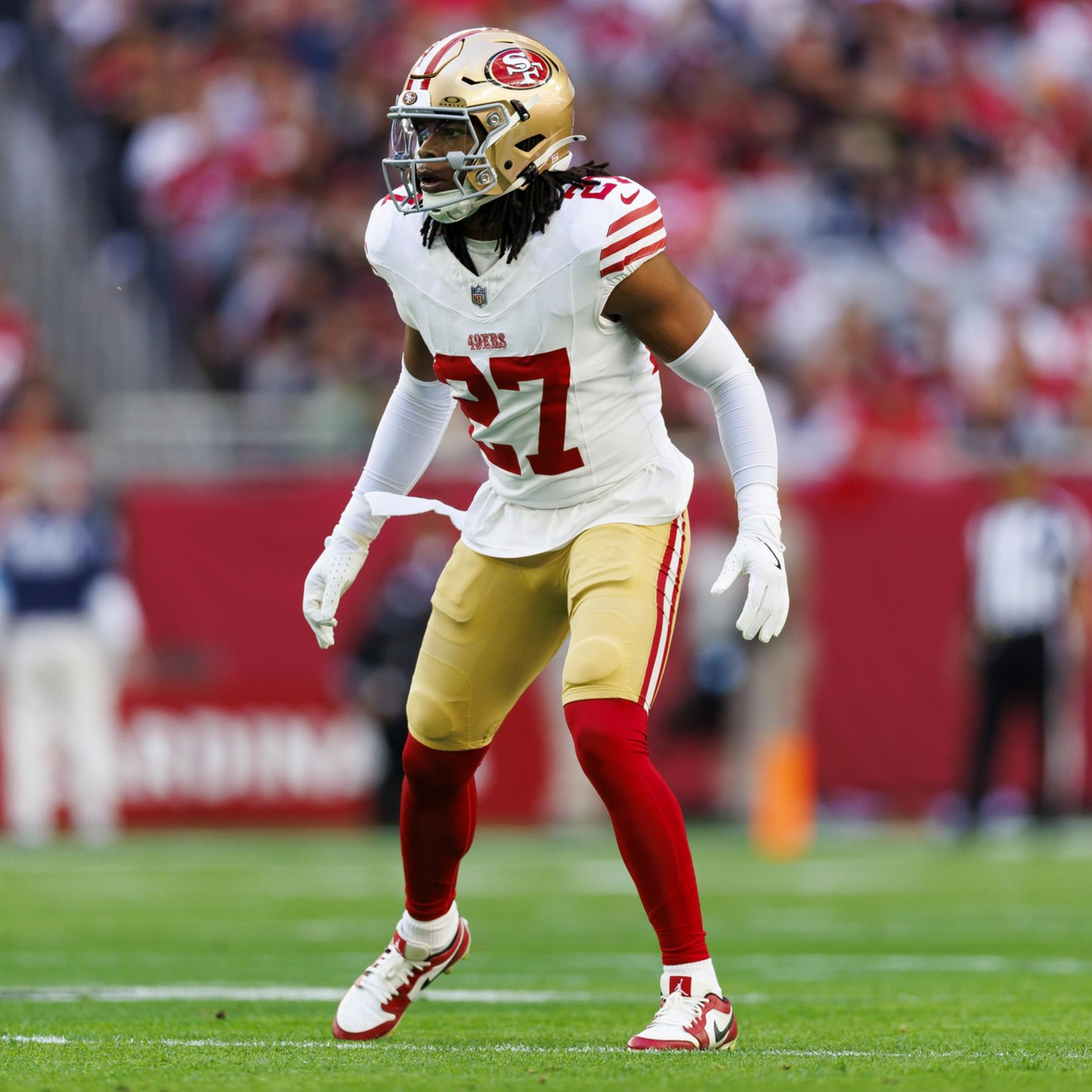 A football player wearing a white and red San Francisco 49ers uniform, number 27, stands ready on the field during a game.