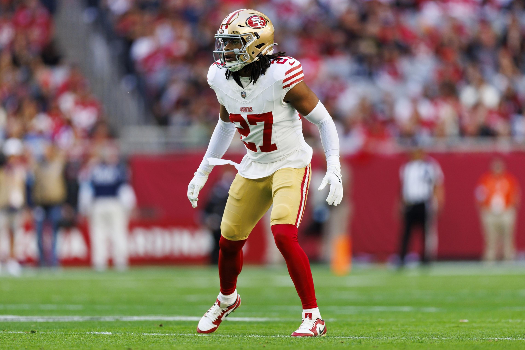 A football player wearing a white and red San Francisco 49ers uniform, number 27, stands ready on the field during a game.