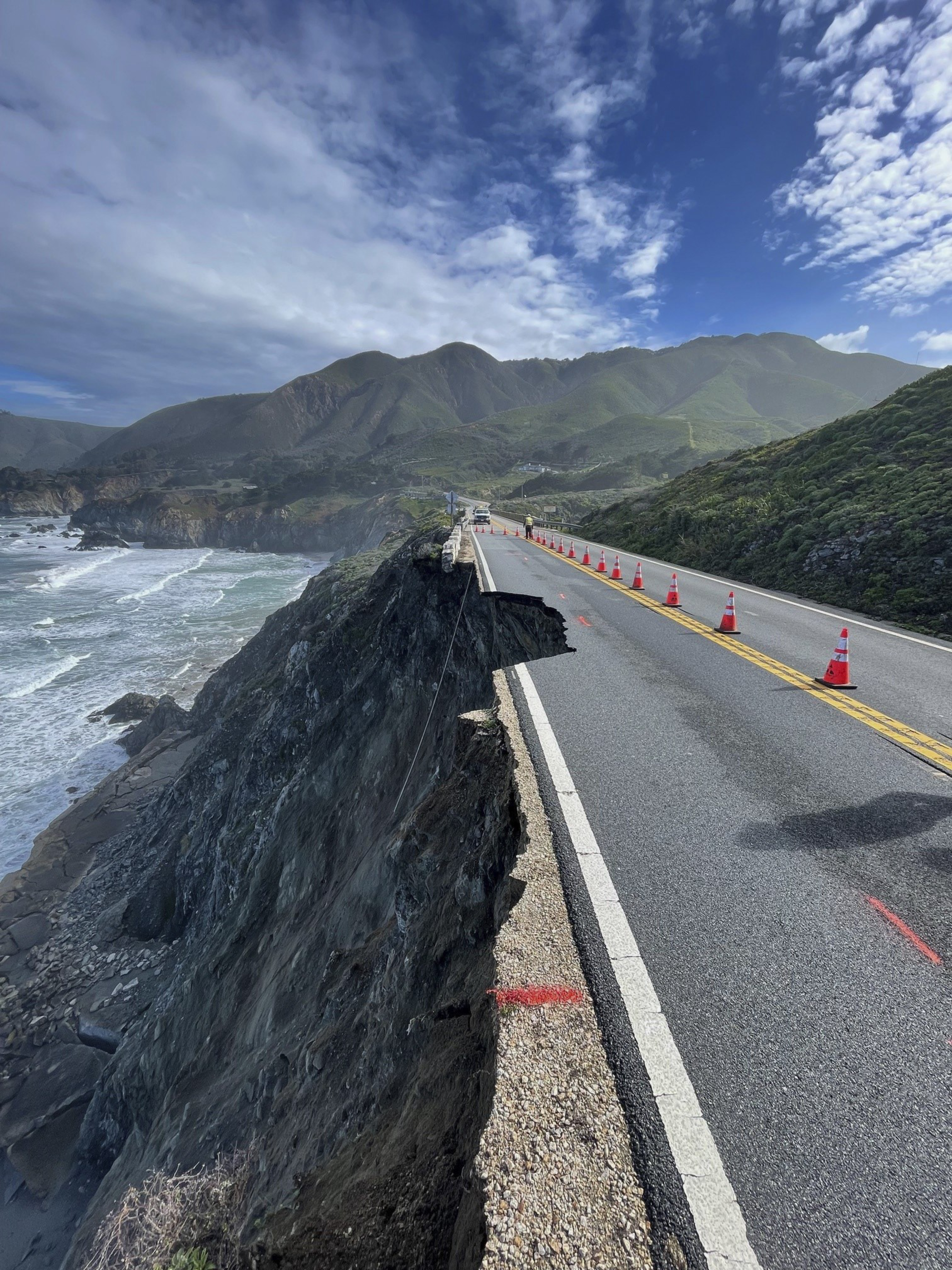 a long shot of a coastal, cliffside highway showing a section of road eroded away