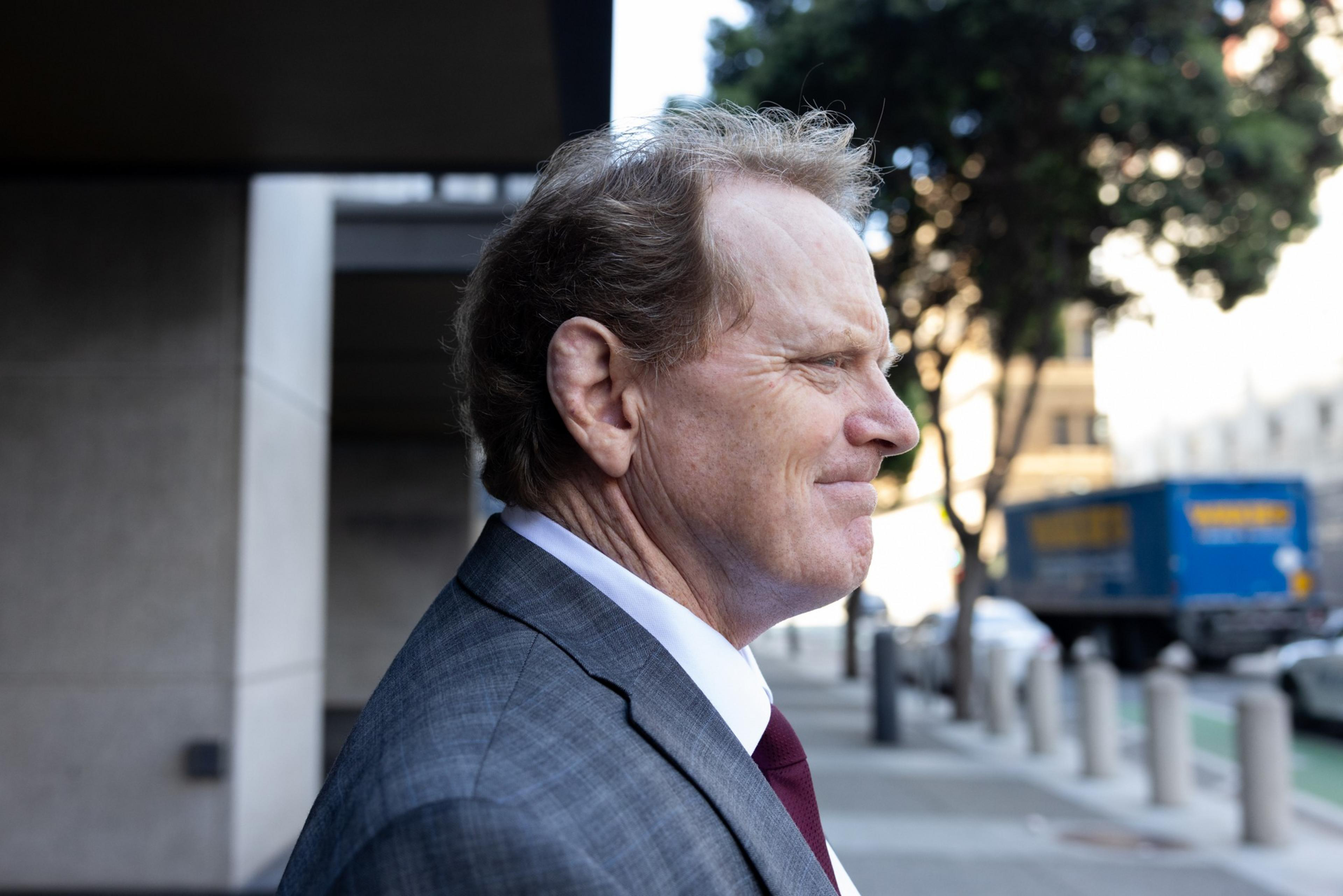 A man in a gray suit and tie leaves a building with a clenched smile