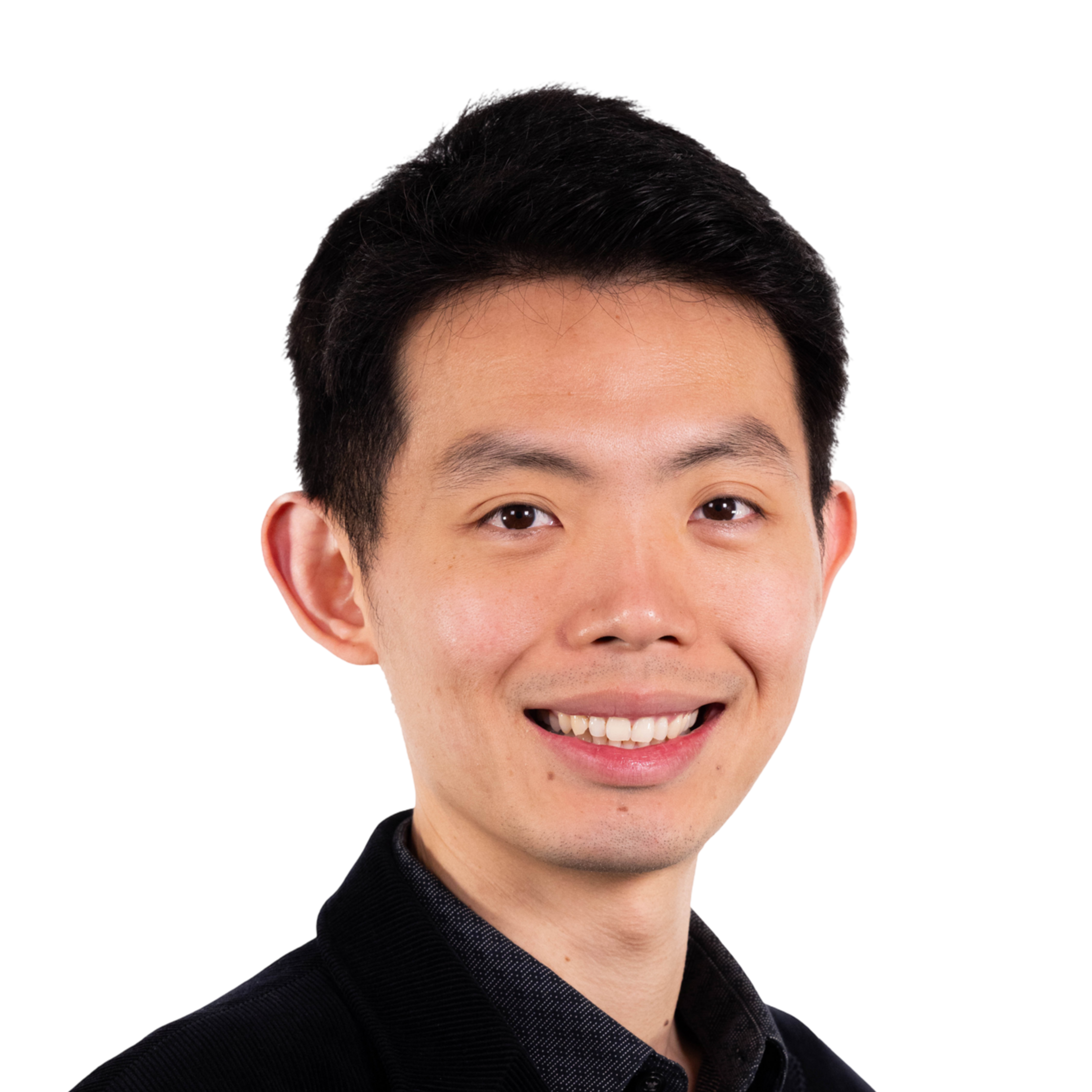A young man with short black hair smiles, wearing a black blazer over a dark button-up shirt, against a plain background.