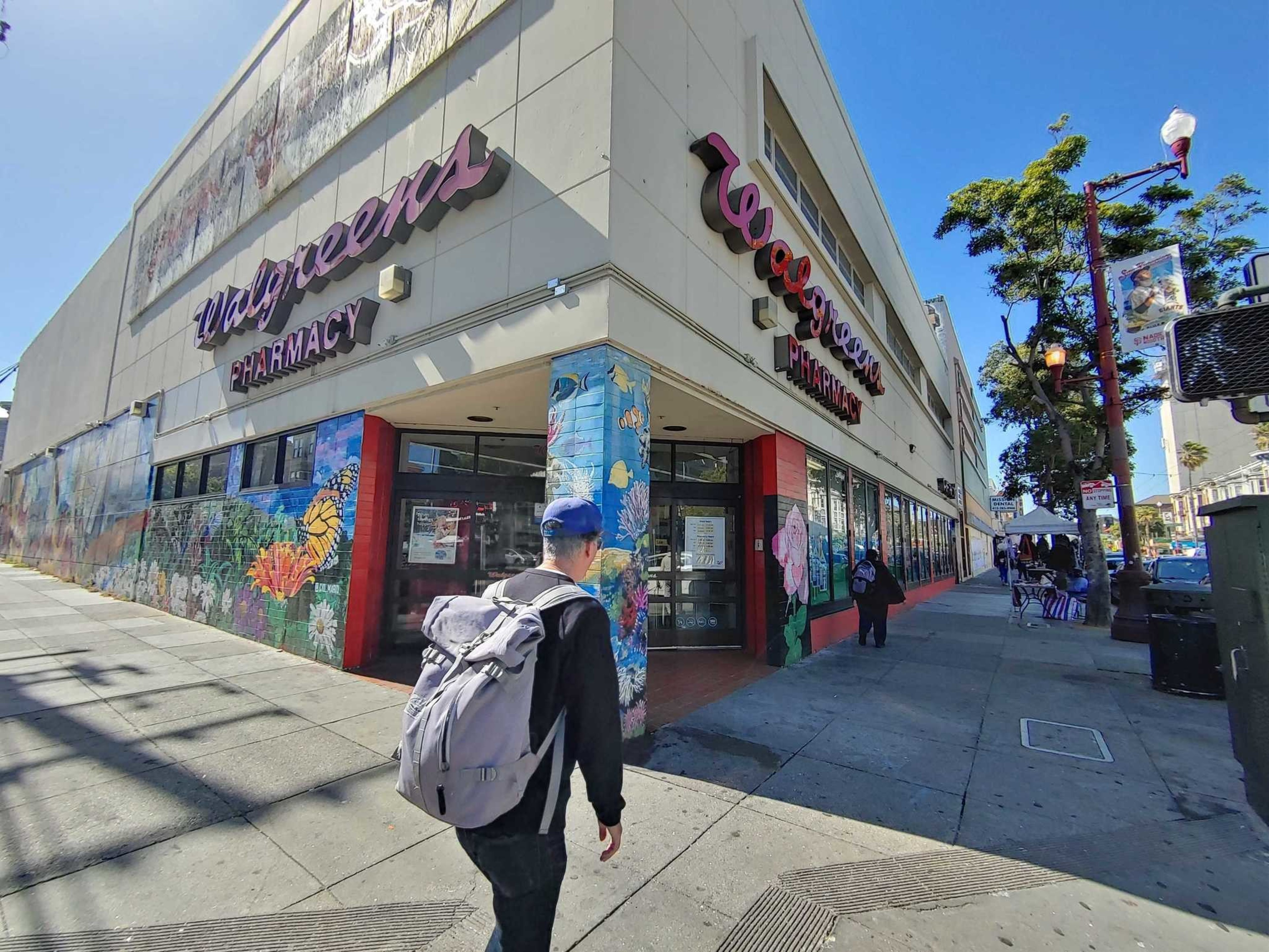 The outside of a drug store, with a person walking outside holding a large gray backpack.